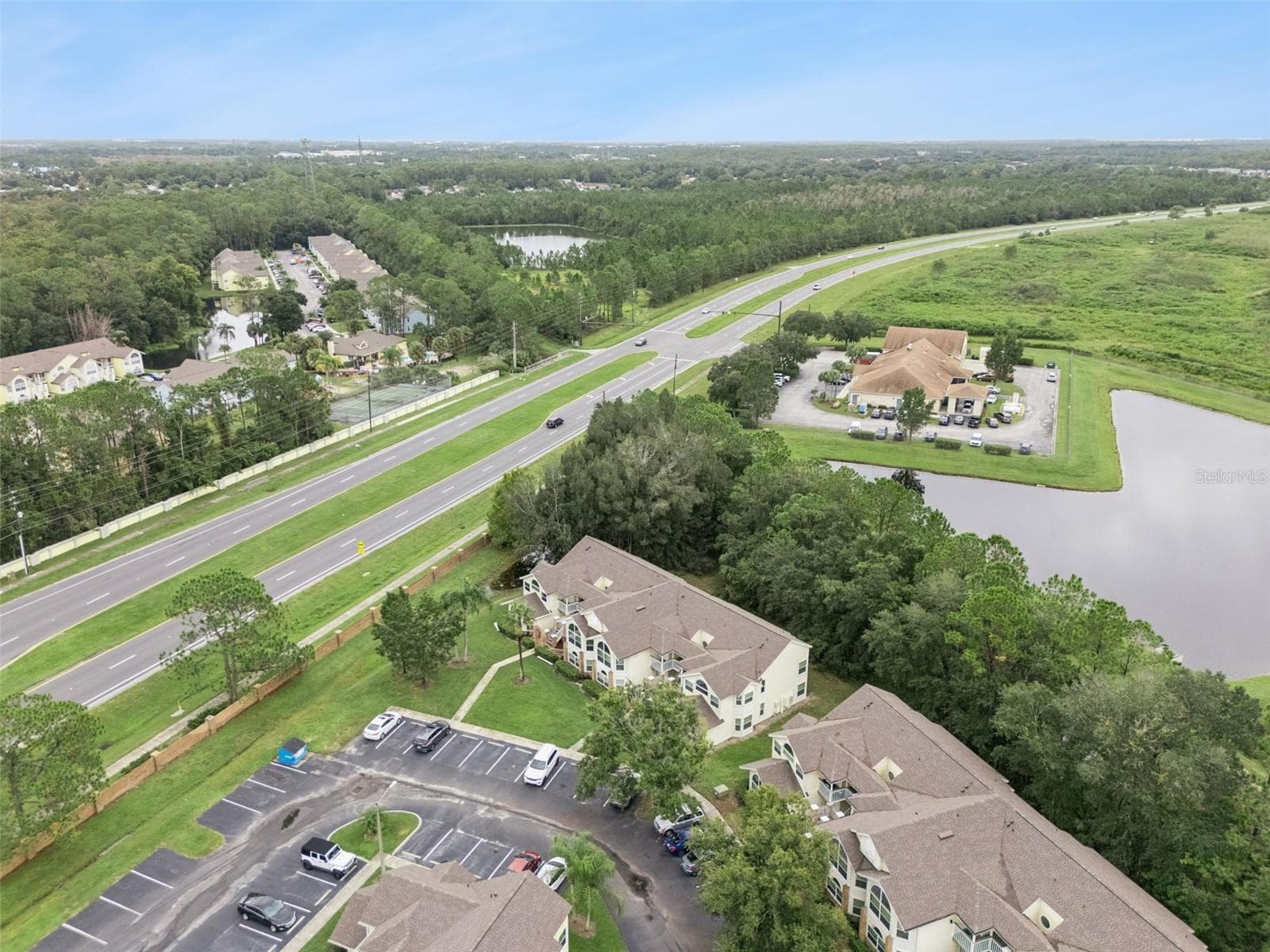 Community Layout Aerial: Angled aerial perspective showcasing the residential building relative to nearby community amenities, water features, and main road - 5017 LAGUNA BAY CIR #100, KISSIMMEE