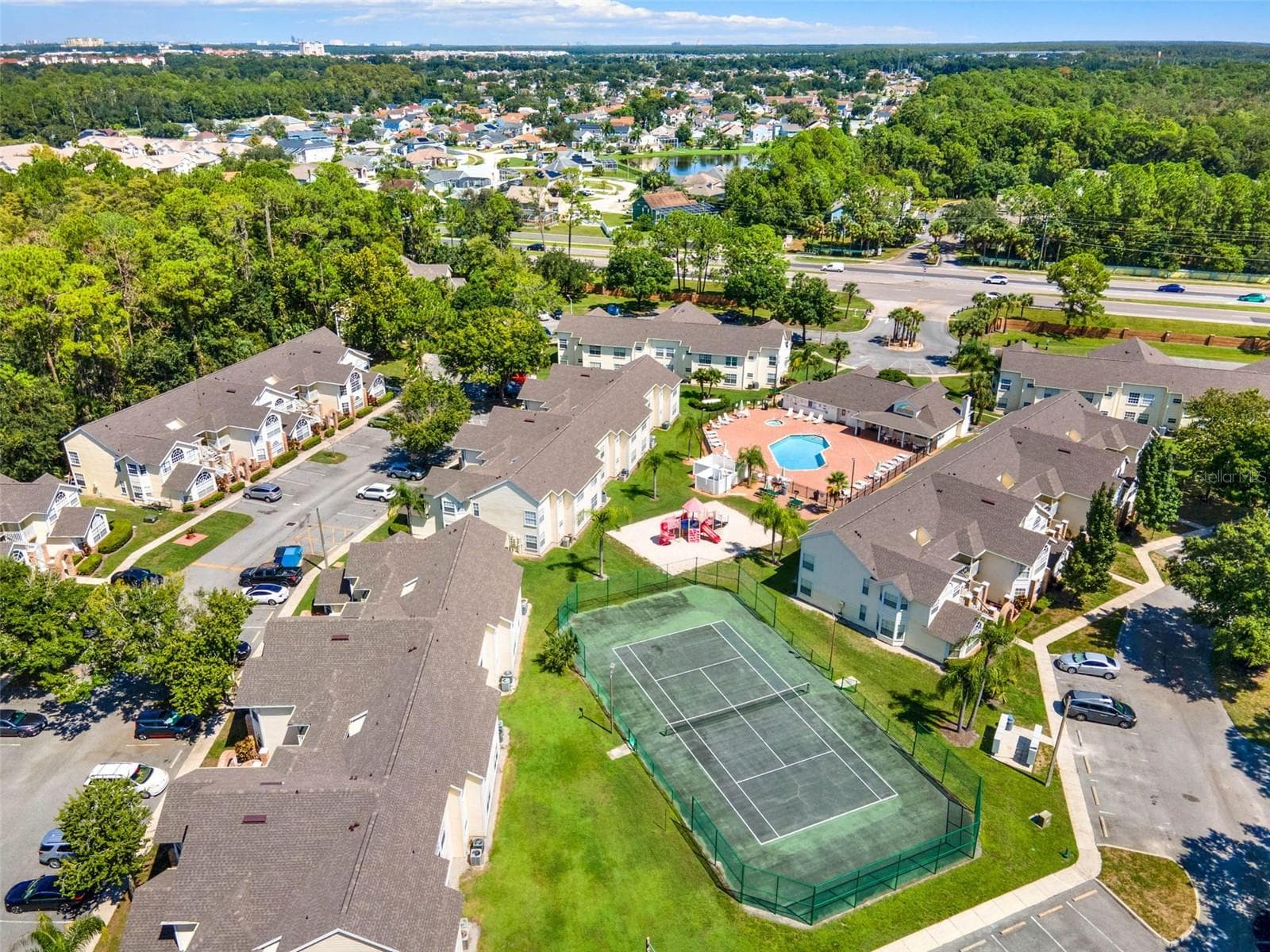 Recreational Facilities Aerial: Elevated aerial view highlighting the outdoor tennis court, resort pool complex, playground area, and manicured green spaces. - 5017 LAGUNA BAY CIR #100, KISSIMMEE