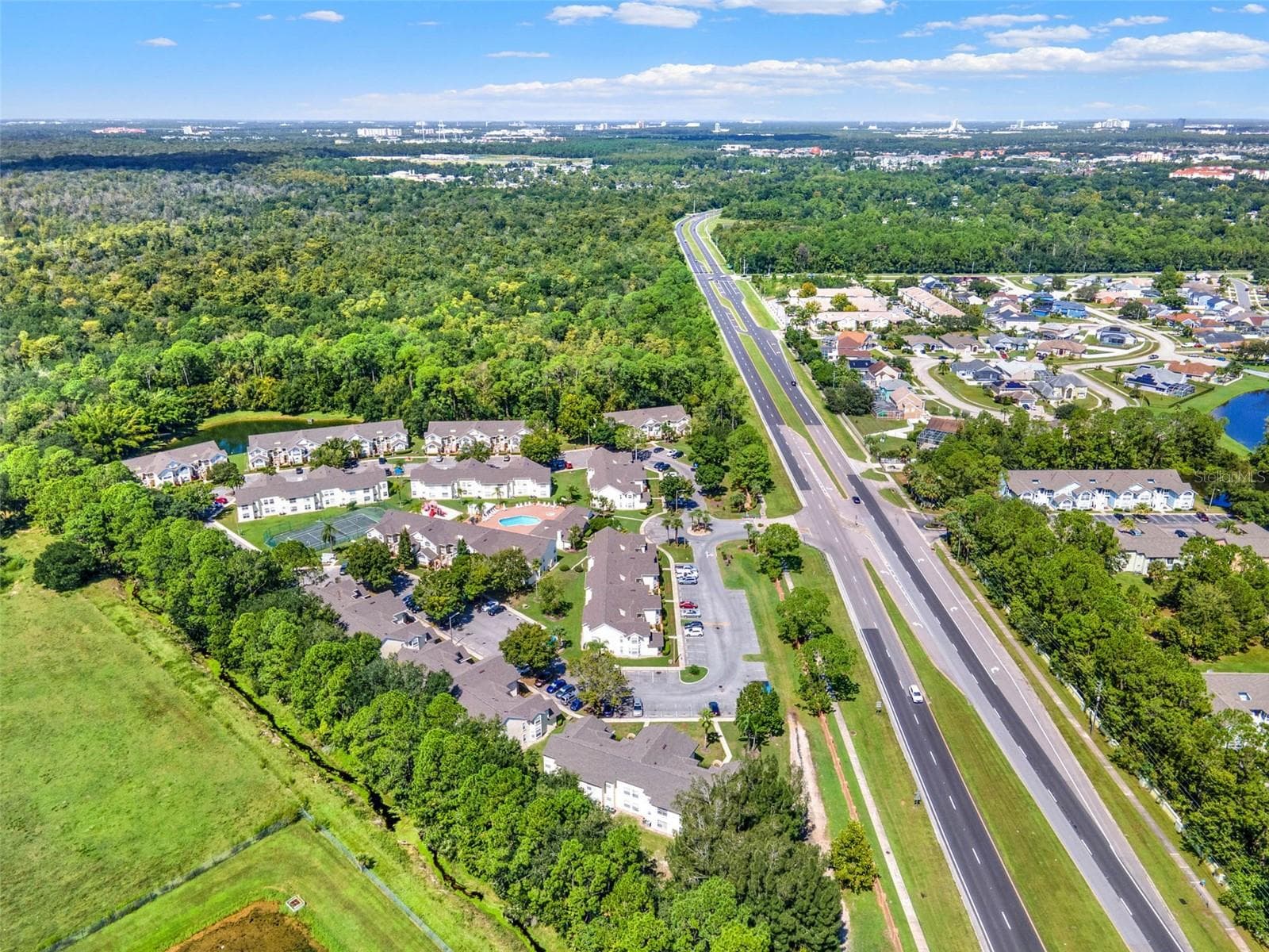 Regional Overview Aerial: High-altitude aerial view showcasing the entire community grounds, surrounding lush foliage, adjacent pond, and convenient highway access. - 5017 LAGUNA BAY CIR #100, KISSIMMEE