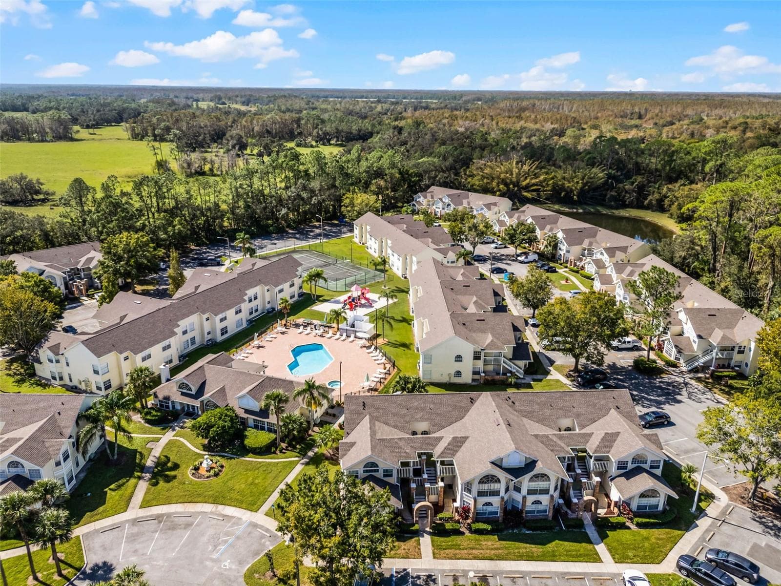 Community Grounds Aerial: High-angle drone perspective emphasizing the expansive community layout, amenity center, and tree-lined perimeter. - 5017 LAGUNA BAY CIR #100, KISSIMMEE