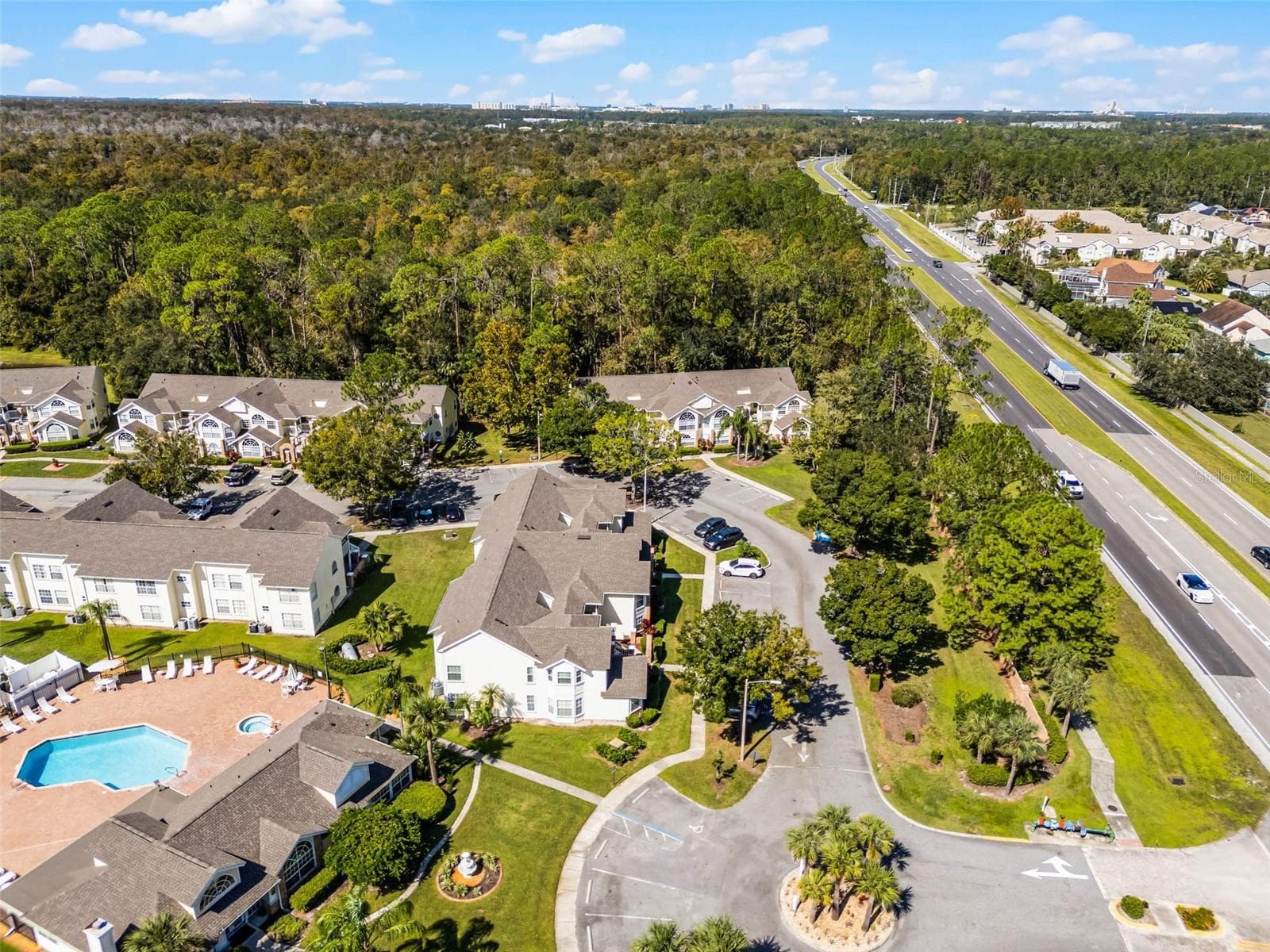Community Entrance & Highway Proximity: Aerial overview featuring the main community drive, entrance roundabout, amenity center, and adjacent major roadway for easy commuting. - 5017 LAGUNA BAY CIR #100, KISSIMMEE