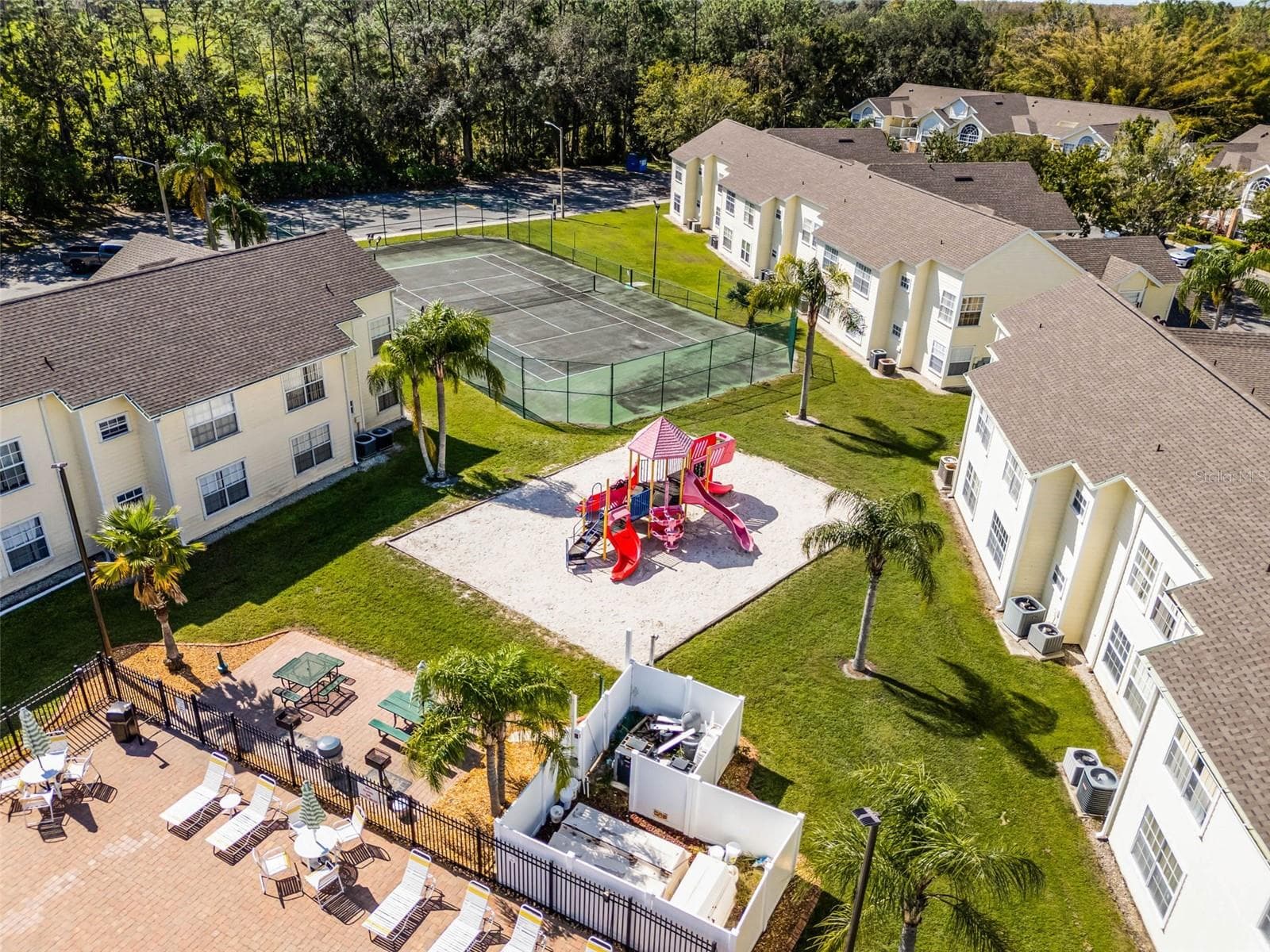 Outdoor Recreational Areas: Focused aerial view showcasing the community playground structure, picnic/grilling zone, fenced tennis court, and manicured green grounds. - 5017 LAGUNA BAY CIR #100, KISSIMMEE