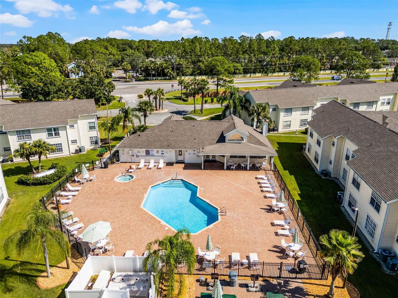 Pool & Spa Complex: Overhead aerial capture of the sparkling resort pool, heated spa, paved lounge deck, covered clubhouse patio, and tropical landscaping. - 5017 LAGUNA BAY CIR #100, KISSIMMEE