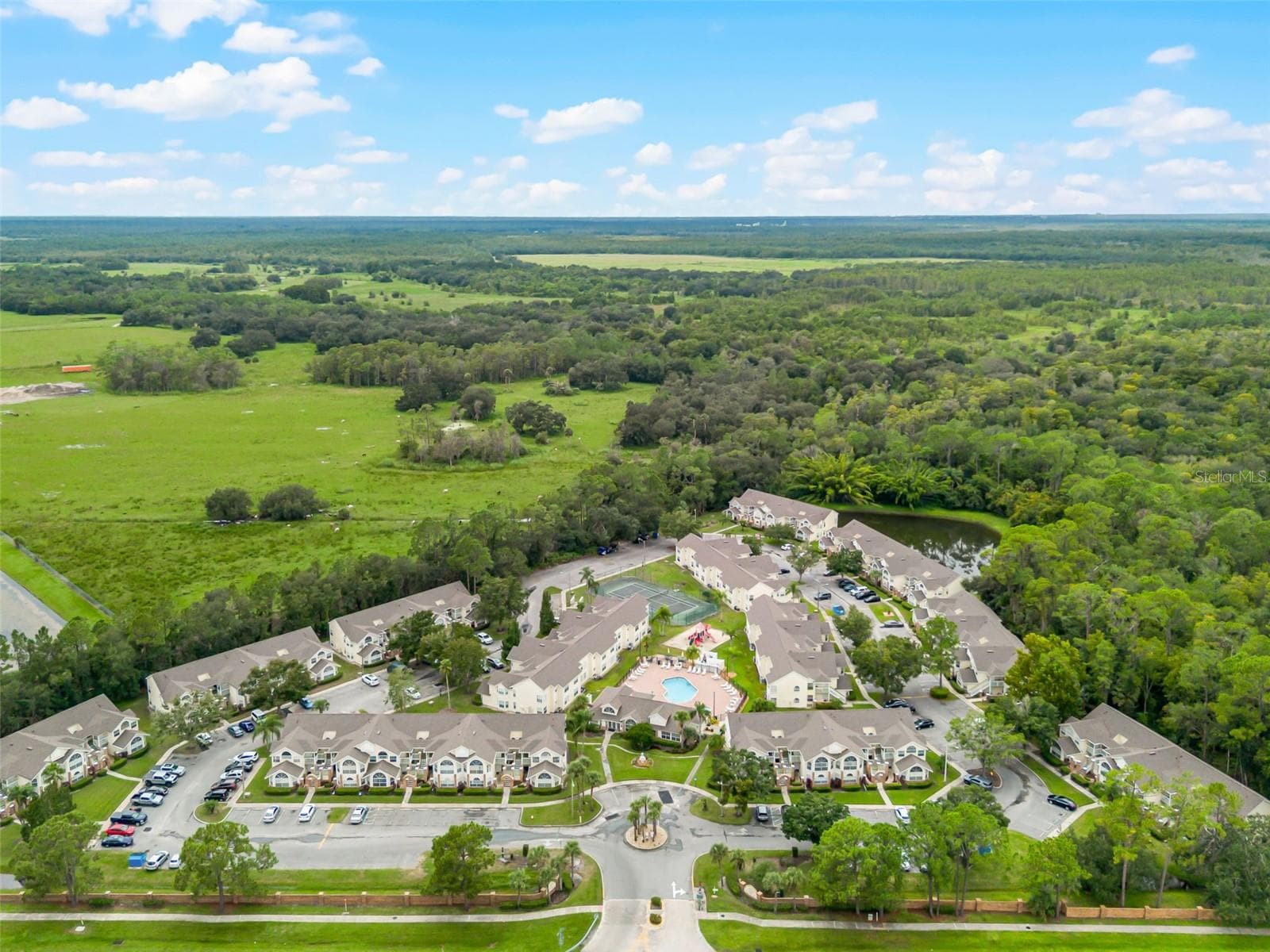 Wide Regional Aerial View: Panoramic high-altitude aerial perspective displaying the entire community layout, lush conservation borders, retention pond, and scenic green horizon. - 5017 LAGUNA BAY CIR #100, KISSIMMEE