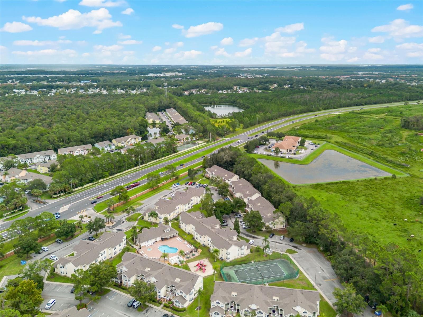 Community & Highway Aerial: High-angle drone shot capturing the full neighborhood grounds, recreational amenities, retention ponds, and direct access to nearby thoroughfares. - 5017 LAGUNA BAY CIR #100, KISSIMMEE