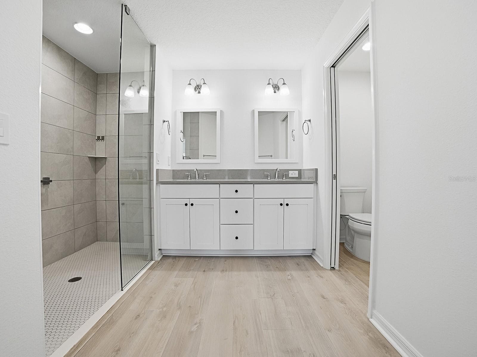 View of primary bathroom from the closet area that are on the left and right of where photographer is standing for this shot. Walk in shower on left and toilet with door on the right side - 1359 DARREN DR, THE VILLAGES