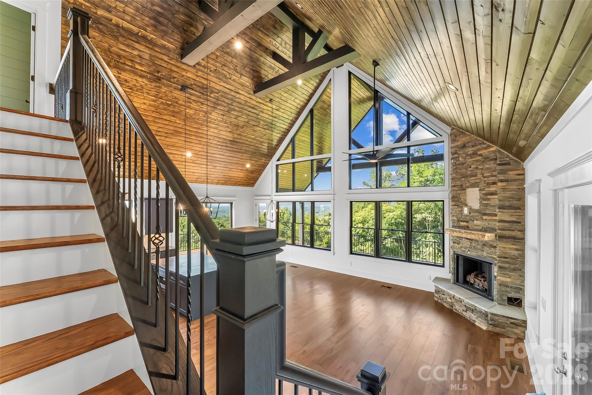 Vaulted wood ceilings, white walls, the stone fireplace, and dark metal stair rails blend natural and contemporary elements for a warm intriguing interior - 4898 Soaring Top Lane, Lenoir