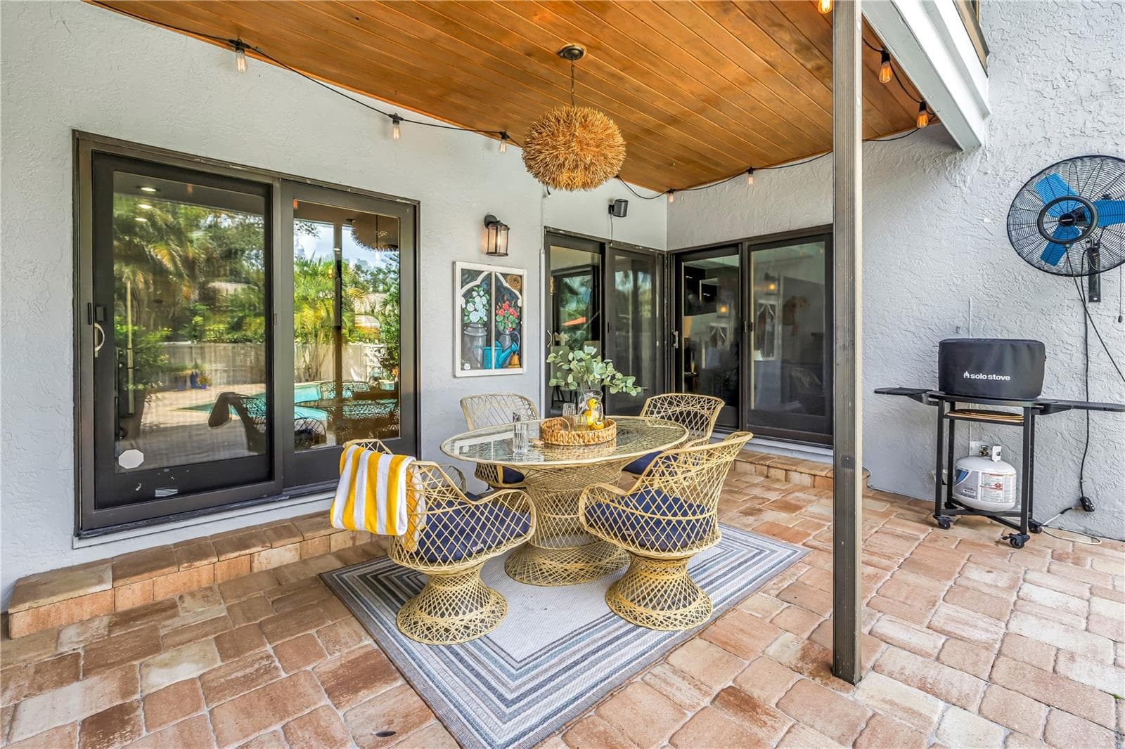 The covered patio overlooks the pool and features a wood-paneled ceiling, ceiling fans, and a designated outdoor grilling area. - 990 SAN CARLOS CT NE, ST PETERSBURG