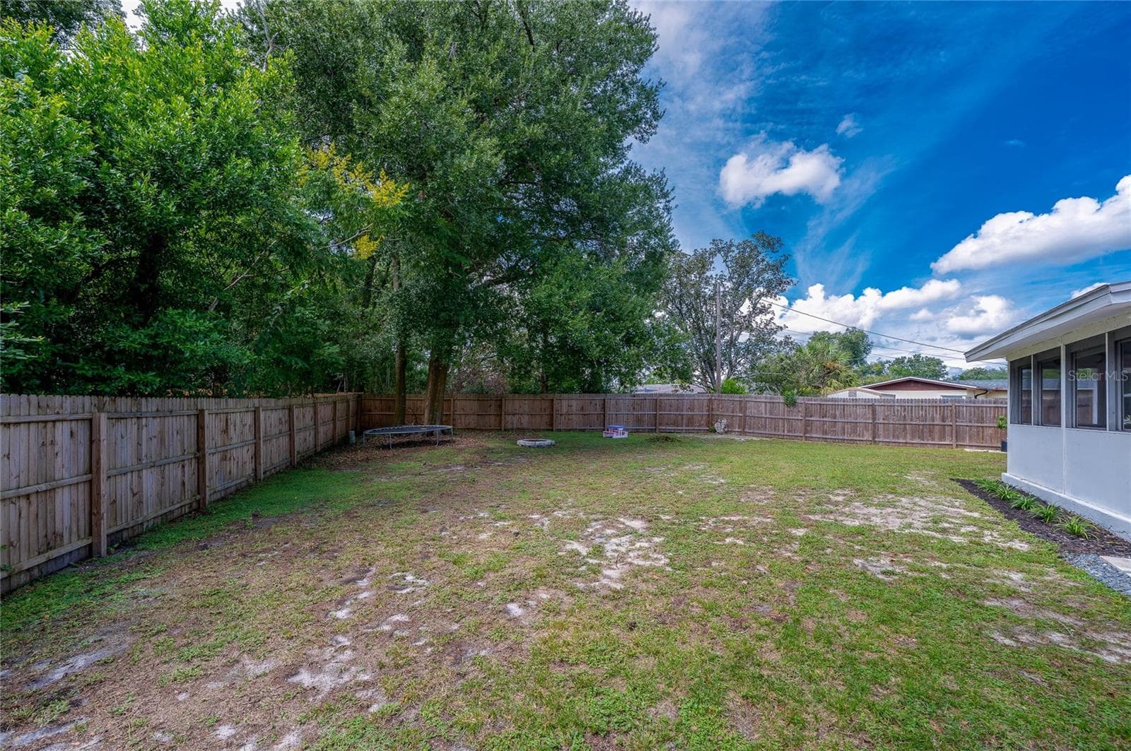 Spacious backyard enclosed by a full wooden privacy fence and lined with mature trees along the perimeter. - 605 E NORMANDY BLVD, DELTONA