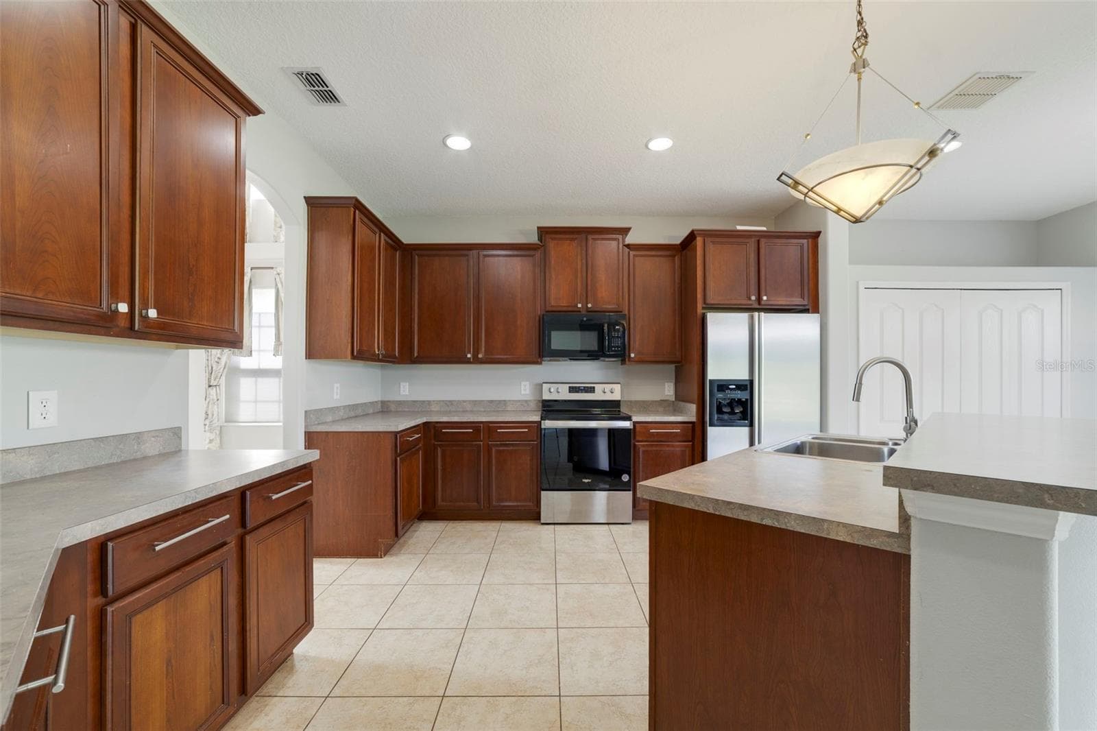 Step through an arched doorway into the spacious Kitchen with ABUNDANT STAGGERED CABINETRY and generous counter space. - 1557 AMARYLLIS CIR, ORLANDO