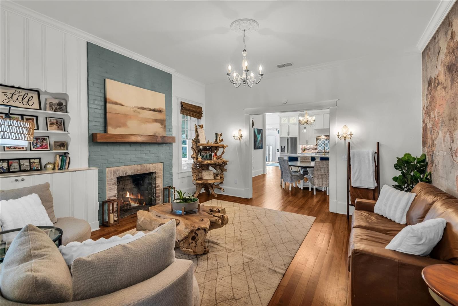 The warm and welcoming Formal Living Room is anchored by a wood-burning brick fireplace accented by a substantial wood mantle and custom painted brick. A custom built in shelf, original wood flooring and chandelier preserve the homes original historic charm and a world map accent wall adds personality. The spacious layout offers a seamless connection to the adjoining dining room and kitchen, creating an effortless flow throughout the home's main living spaces. - 234 N LAKEVIEW AVE, WINTER GARDEN