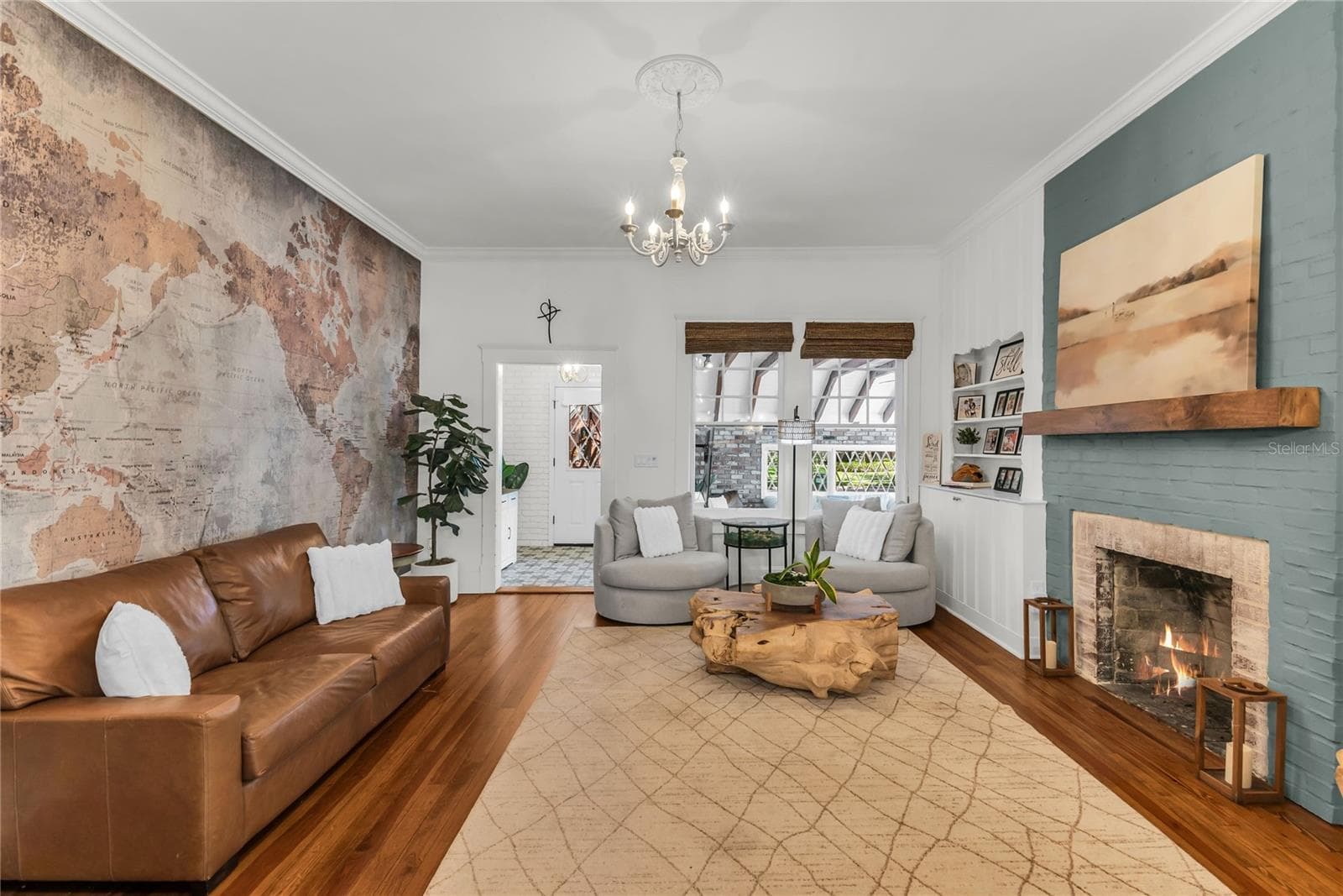 The warm and welcoming Formal Living Room is anchored by a wood-burning brick fireplace accented by a substantial wood mantle and custom painted brick. A custom built in shelf, original wood flooring and chandelier preserve the homes original historic charm and a world map accent wall adds personality. The spacious layout offers a seamless connection to the adjoining dining room and kitchen, creating an effortless flow throughout the home's main living spaces. - 234 N LAKEVIEW AVE, WINTER GARDEN