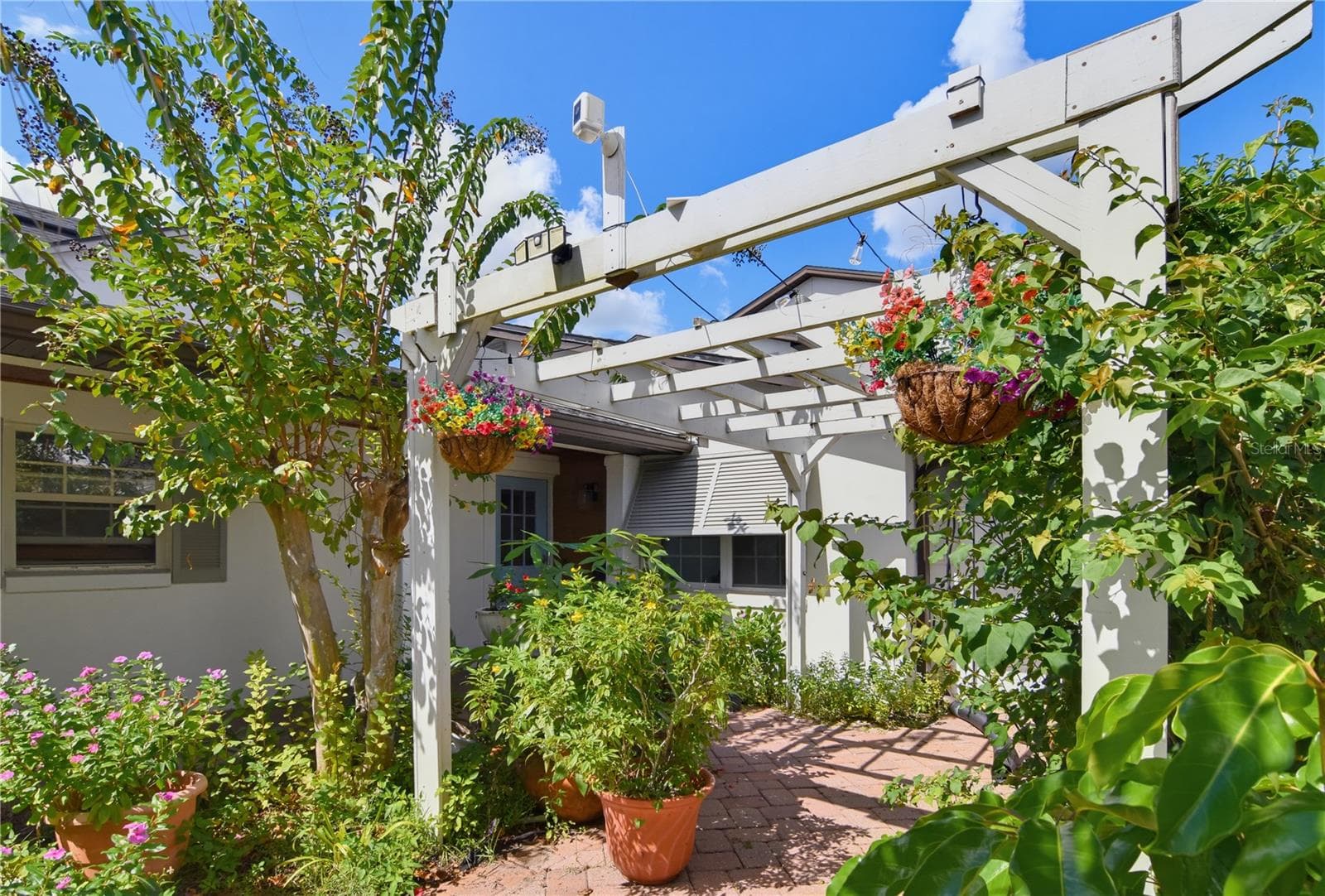 Charming landscaped front courtyard featuring a white pergola and a brick-paved walkway. - 1611 CHESTNUT AVE, WINTER PARK