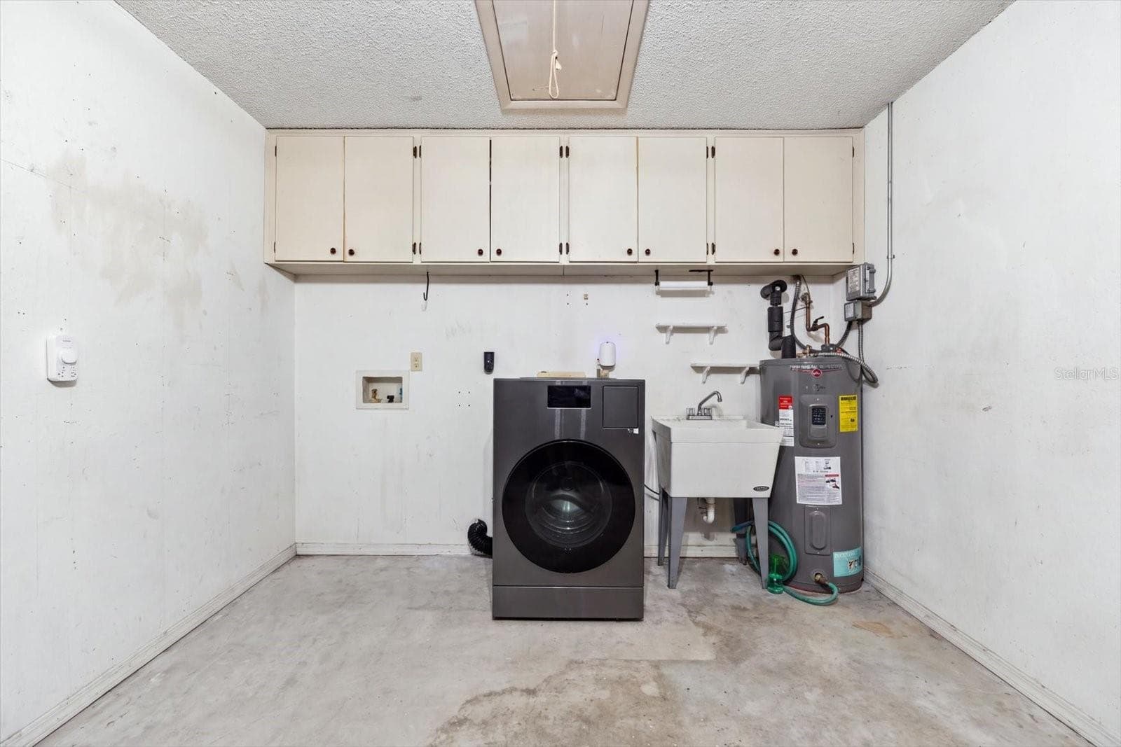 Garage with storage cabinets, washer/dryer combo, utility sink and water heater (2022). Newer Hurricane rated garage door 2023 - 1307 STONEHAVEN LN, DUNEDIN