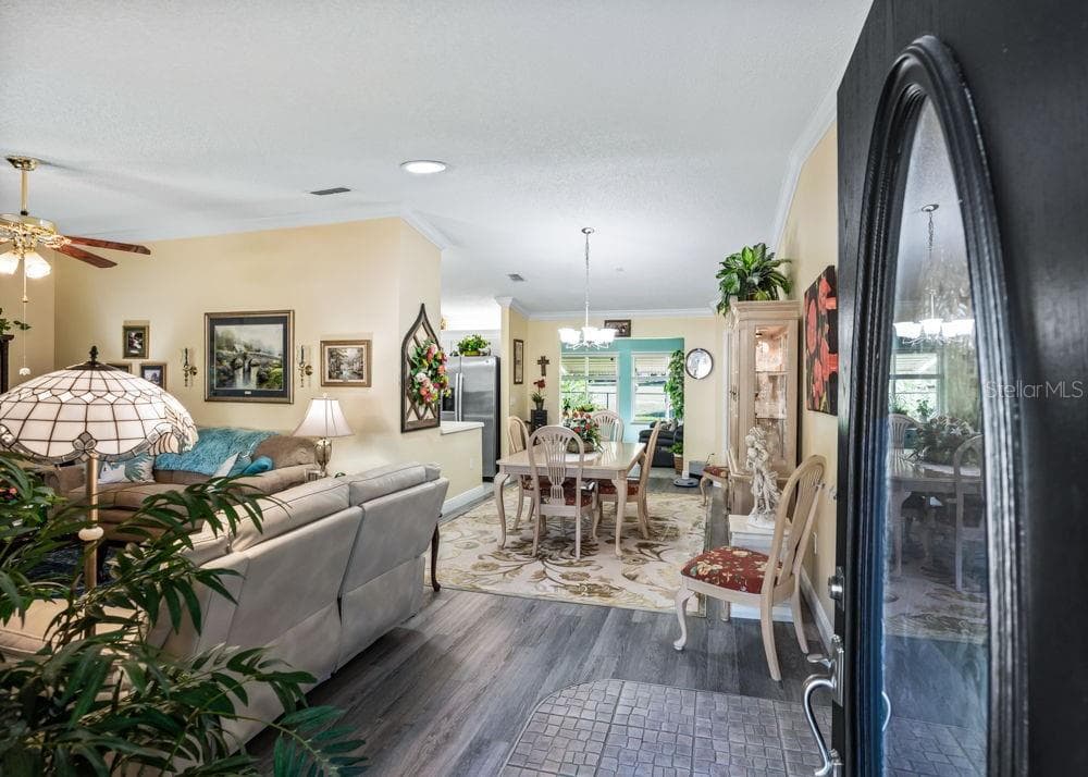 Welcoming entry opens to a bright living and dining area featuring wood-look vinyl flooring, crown molding, and soft neutral tones. The open layout offers an inviting flow, with views toward the kitchen and sunlit rear living space. - 17909 SE 99TH AVE, SUMMERFIELD