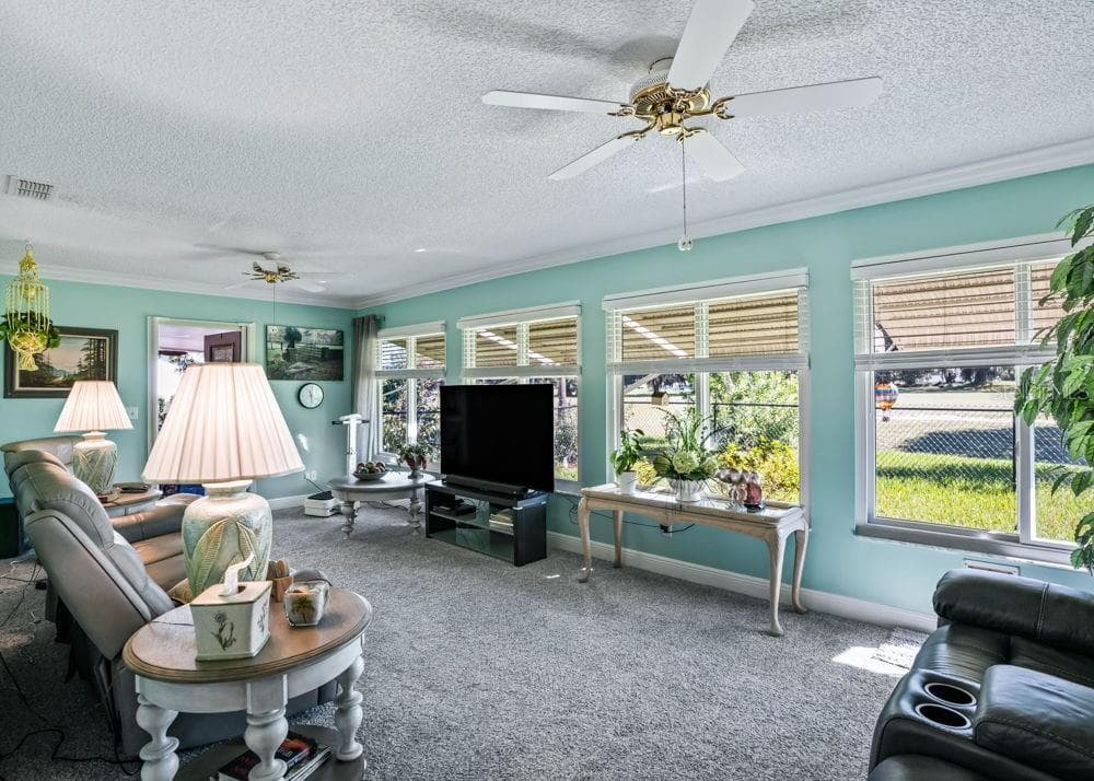 The spacious Florida room features a wall of windows that fills the space with natural light and offers views of the surrounding greenery. Soft aqua walls, crown molding, carpeting, and two ceiling fans create an inviting setting for relaxing or entertaining. - 17909 SE 99TH AVE, SUMMERFIELD