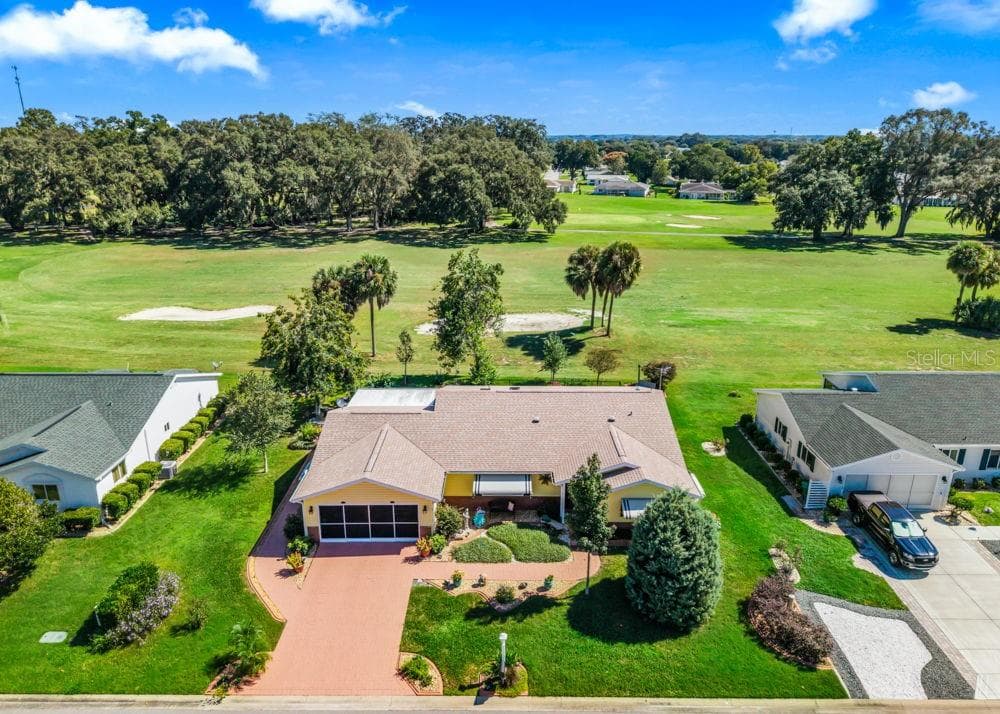 This aerial view highlights the home’s prime setting directly on The Links golf course, with sweeping fairway views and mature trees beyond the backyard. A brick-paver driveway, screened two-car garage, and beautifully landscaped grounds enhance the home’s curb appeal. - 17909 SE 99TH AVE, SUMMERFIELD