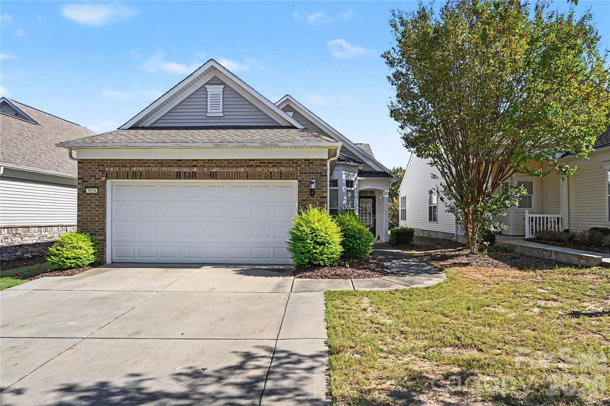 Another view of the home showing the long driveway, brick front, mature landscaping, and front porch. - 3054 Azalea Drive, Indian Land