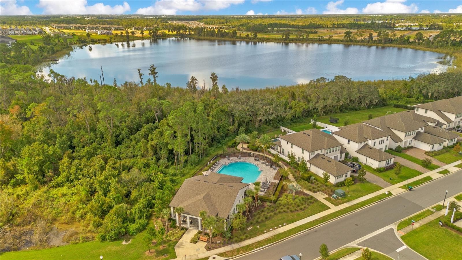 Aerial view of the community amenity area with a pool, clubhouse and lake backdrop. - 17600 LAKE STAR RD, WINTER GARDEN
