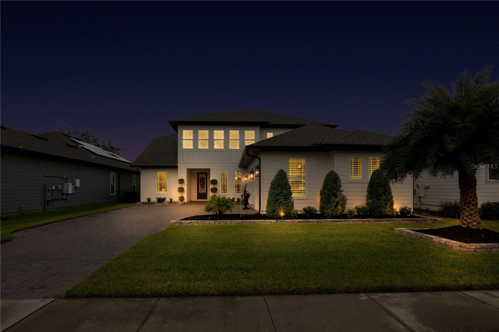 Twilight view of the paver driveway and front entrance with warm exterior lighting. - 17600 LAKE STAR RD, WINTER GARDEN