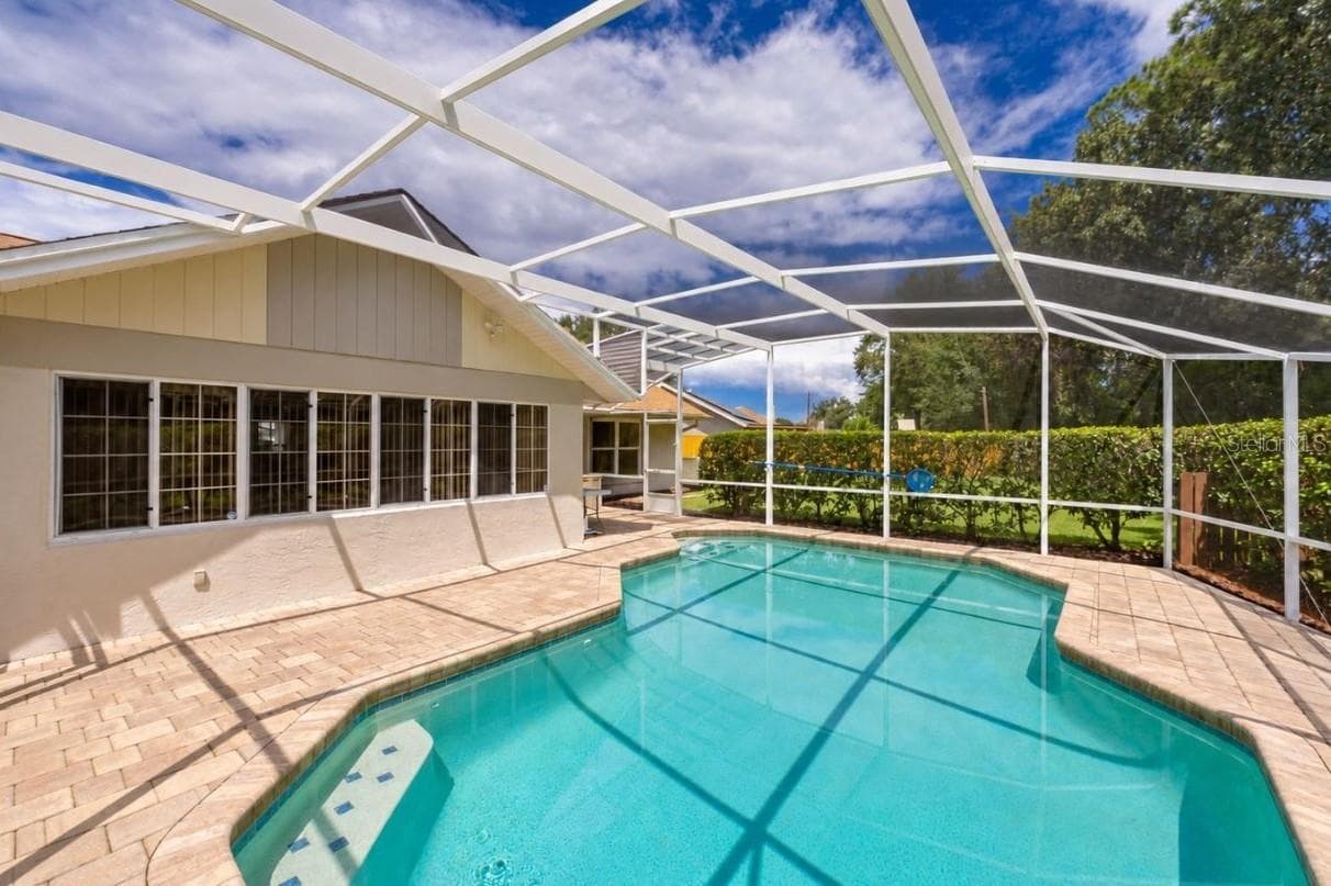 Alternate angle of the screened swimming pool enclosure, highlighting the extensive paved deck and home exterior. - 4669 SECRET RIVER TRL, PORT ORANGE