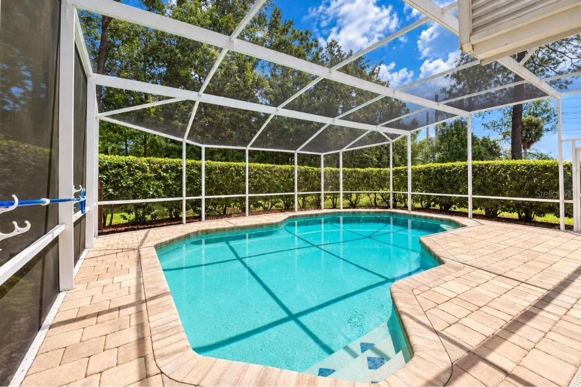 Screened-in pool deck area featuring a paved surround and private hedge line along the perimeter. - 4669 SECRET RIVER TRL, PORT ORANGE