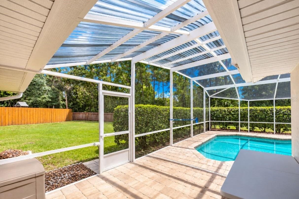 Paved patio area leading to a screened-in swimming pool enclosure with views of the grassy lawn. - 4669 SECRET RIVER TRL, PORT ORANGE
