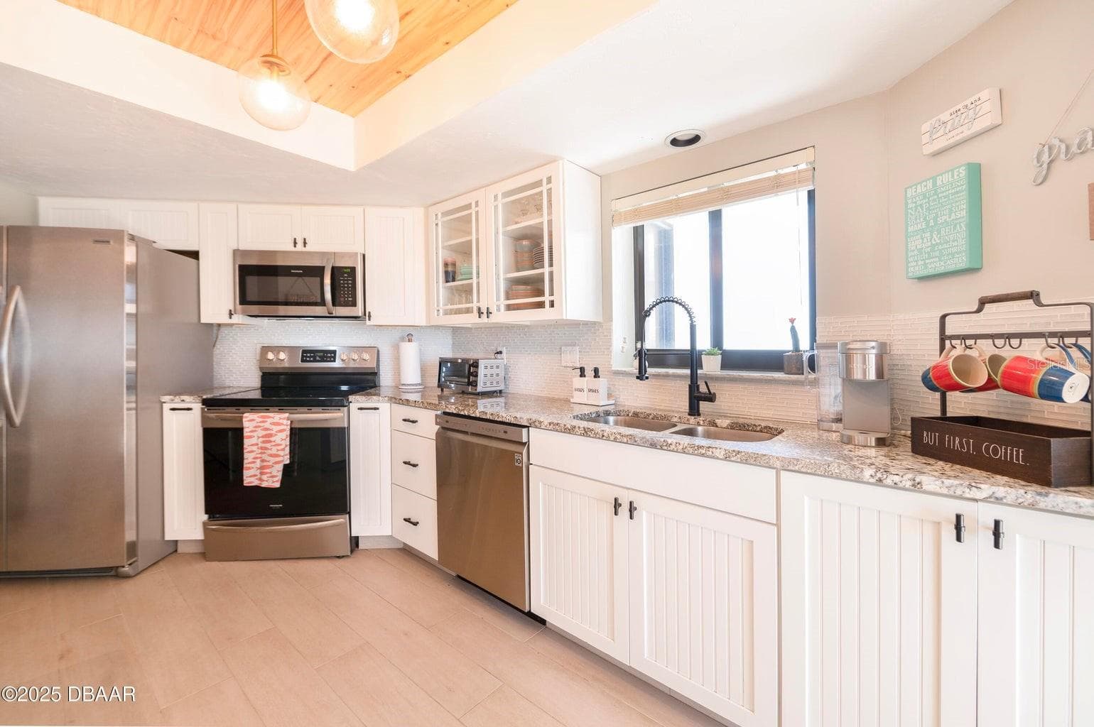 This thoughtfully designed kitchen showcases stainless steel appliances, generous counter space, white cabinetry with contrasting hardware, and a double-basin sink with a modern black faucet. - 3855 S ATLANTIC AVE #401, DAYTONA BEACH