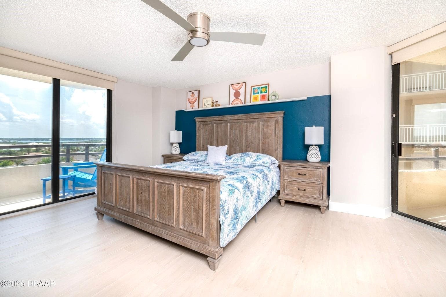 This spacious primary suite features a striking blue accent wall, contemporary ceiling fan, and sliding glass doors opening to a private balcony with scenic inland views. - 3855 S ATLANTIC AVE #401, DAYTONA BEACH