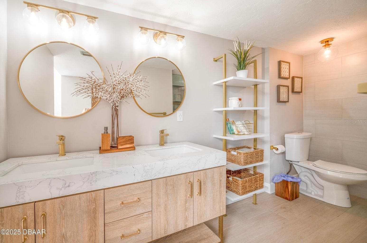 The spacious double vanity showcases marble-look countertops with integrated sinks, warm wood-tone cabinetry, stylish gold accents, and open shelving for convenient storage. - 3855 S ATLANTIC AVE #401, DAYTONA BEACH