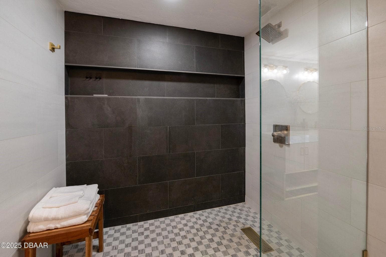 : This spacious walk-in shower features a striking dark tile accent wall, contrasting light tile surrounds, a rainfall showerhead, built-in storage niche, and sleek glass partition for a contemporary, spa-inspired feel. - 3855 S ATLANTIC AVE #401, DAYTONA BEACH