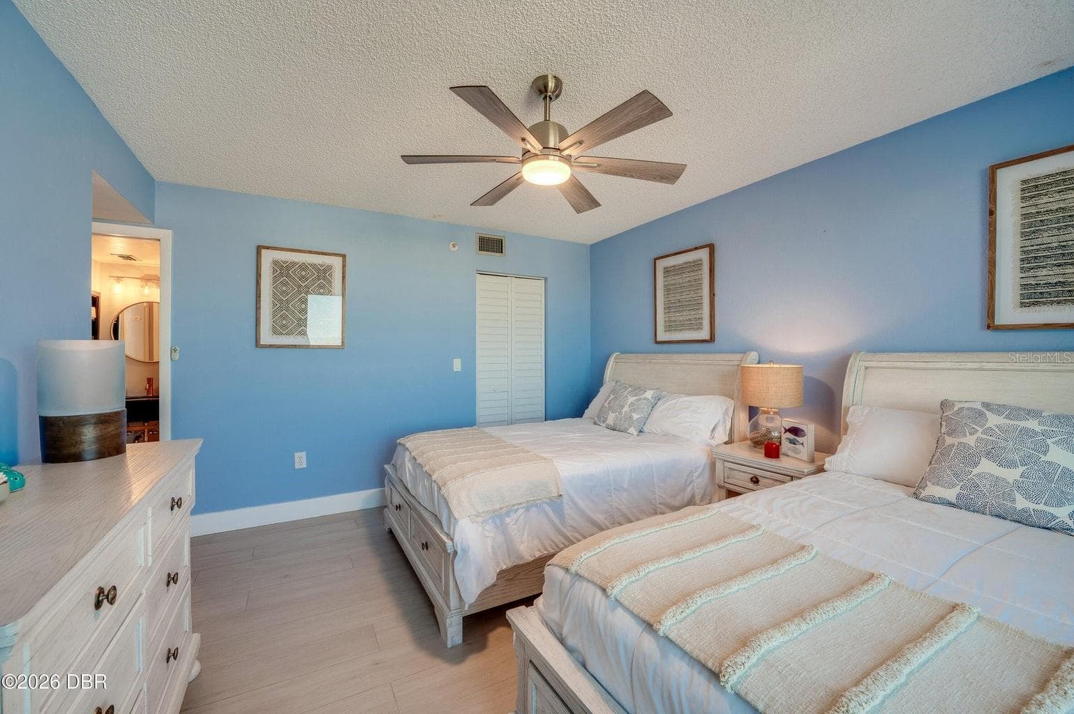 This inviting guest bedroom features soft blue walls, a contemporary ceiling fan, and coastal-inspired finishes, creating a bright and comfortable space for guests. - 3855 S ATLANTIC AVE #401, DAYTONA BEACH