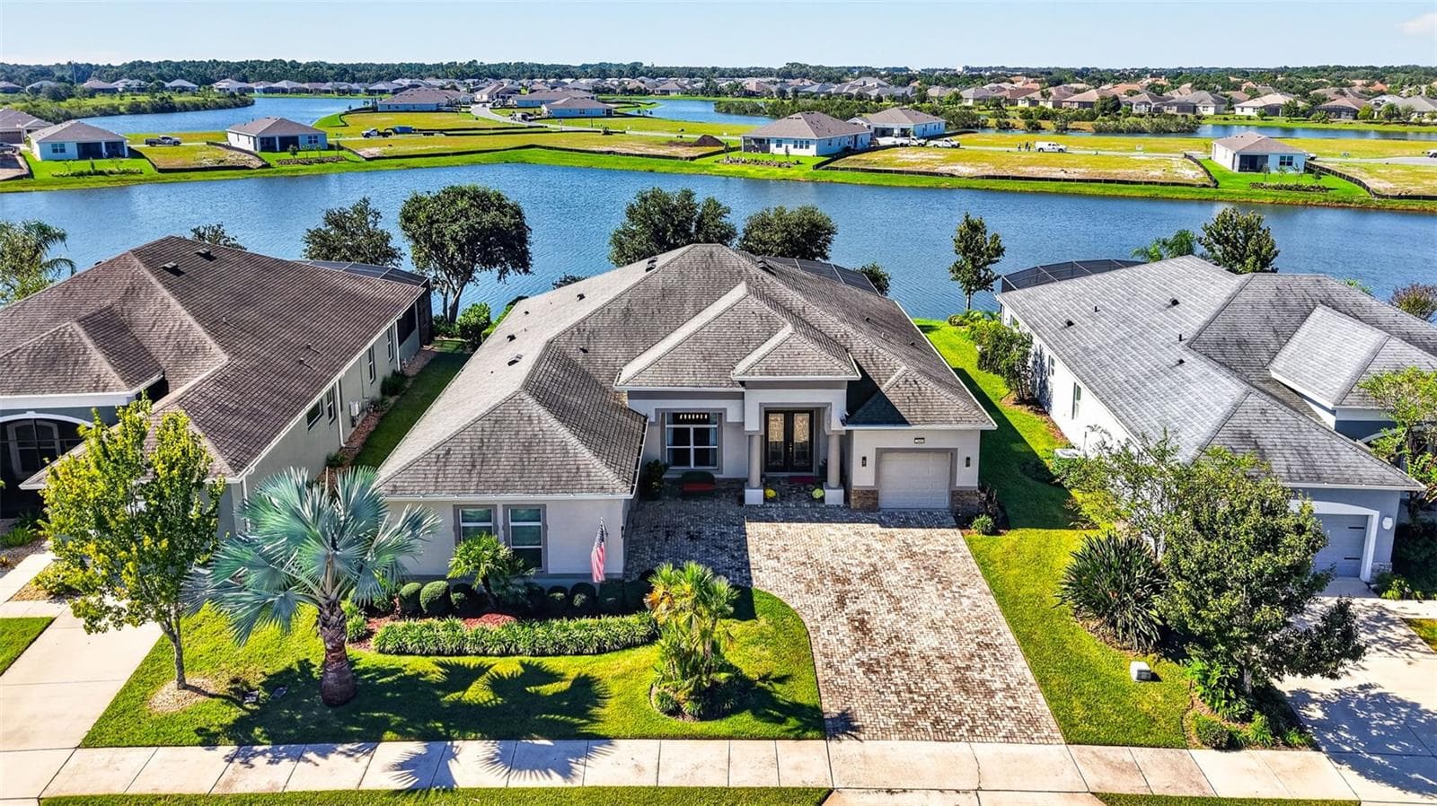 An aerial drone view highlights the front exterior of the home, framed by a serene lake backdrop. - 2444 PAWTUCKET PASS, MOUNT DORA
