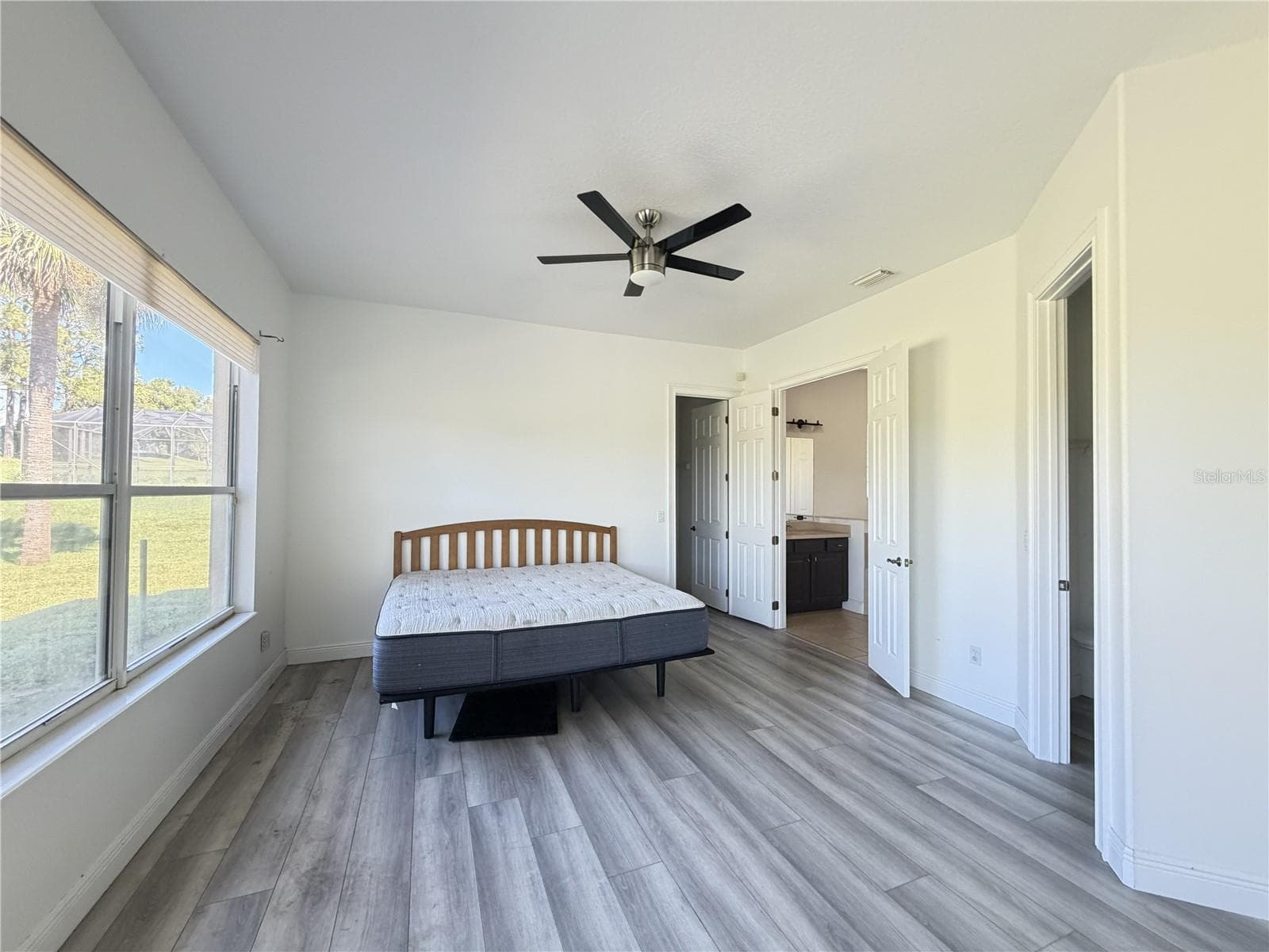 Main-floor primary bedroom with luxury vinyl flooring, ceiling light fan, 2 walk-in closets, and ensuite bathroom. - 39539 HARBOR HILLS BLVD, LADY LAKE