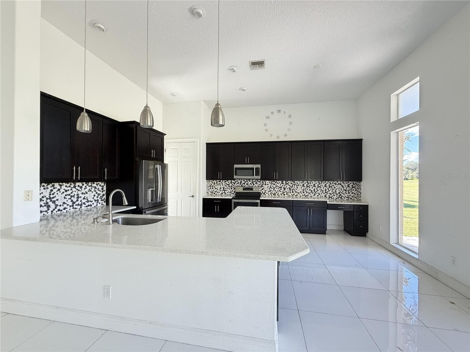 Open bright kitchen with pendant lighting, quartz countertops, decorative backsplash, counter seating, and desk area. - 39539 HARBOR HILLS BLVD, LADY LAKE