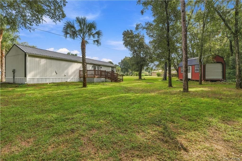 Backyard & Storage Building – Spacious backyard featuring mature trees, open lawn, wooden deck & a distinctive RED DETACHED STORAGE BUILDING w/metal roof & roll-up door. - 6230 W GLEN ROBBIN CT, CRYSTAL RIVER