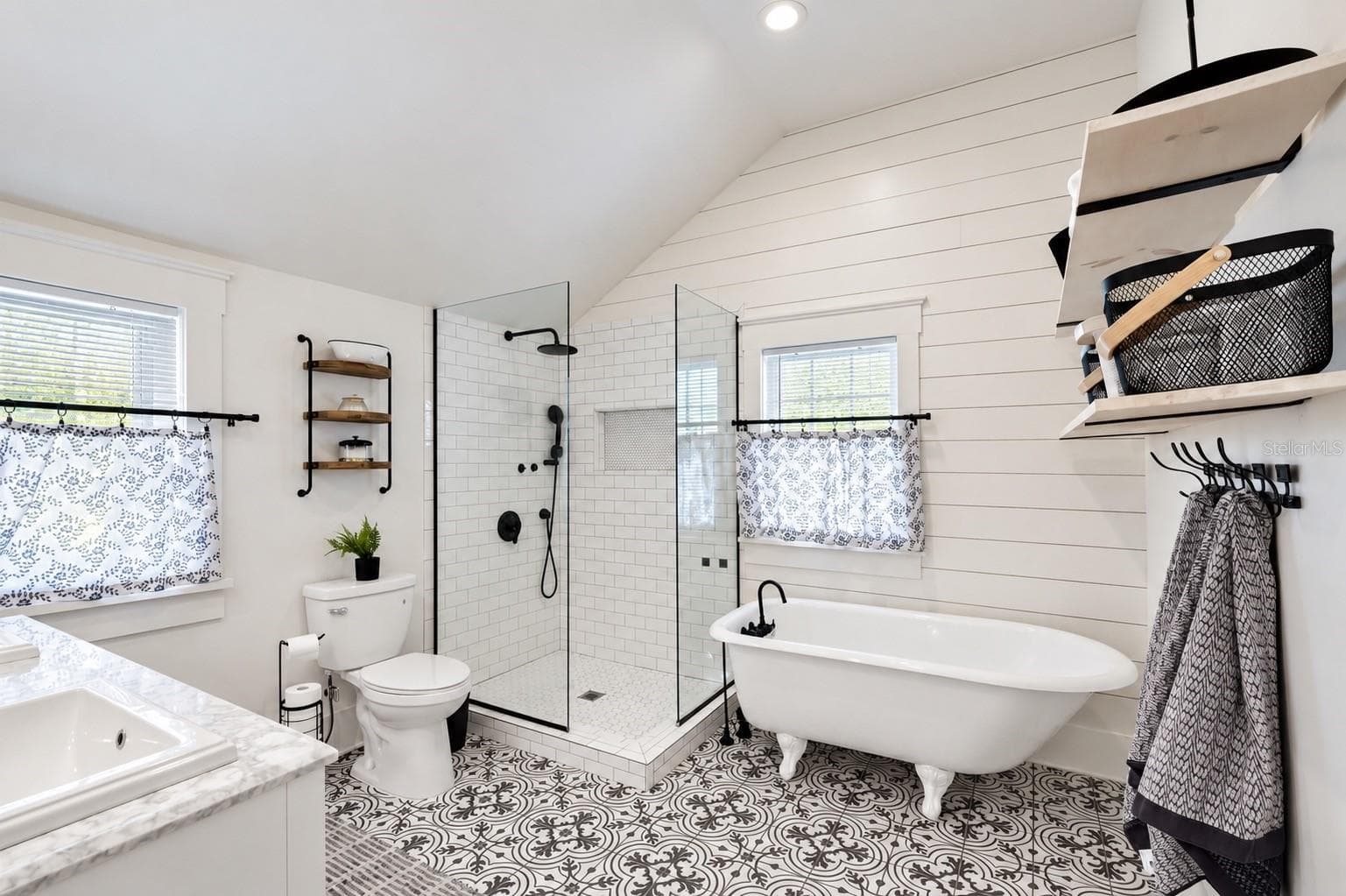 Beautifully updated upstairs bathroom conveniently located between both bedrooms, featuring a charming clawfoot soaking tub, spacious glass-enclosed walk-in shower, stylish patterned tile flooring, shiplap walls, and elegant black fixtures. - 1901 10TH ST, ST CLOUD