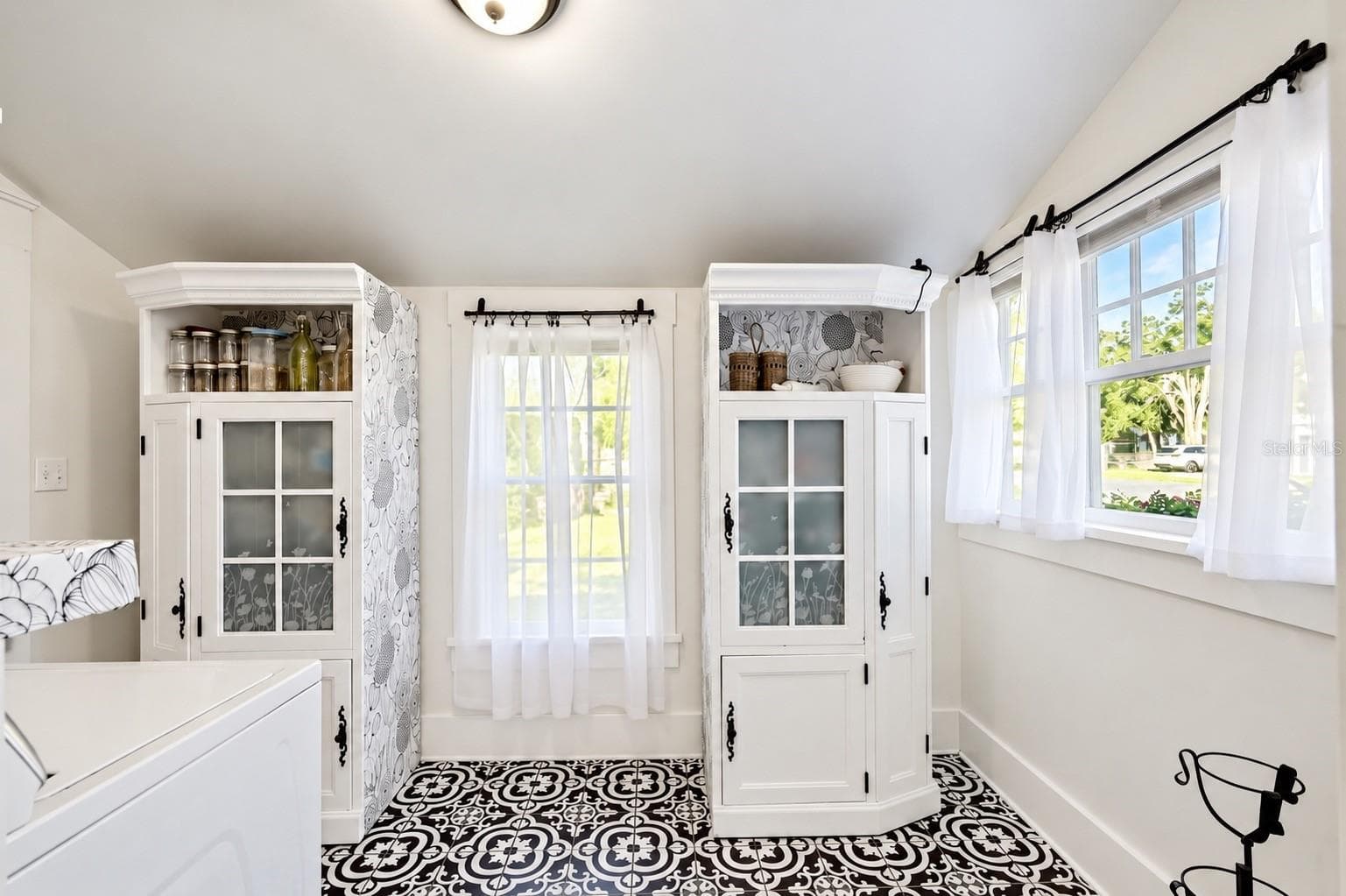 INDOOR LAUNDRY ROOM featuring beautiful patterned tile flooring, abundant natural light, and decorative storage cabinets. Convenient access through the adjoining full downstairs bathroom leads to the spacious FENCED BACKYARD AND BARN, offering both functionality and farmhouse charm! - 1901 10TH ST, ST CLOUD