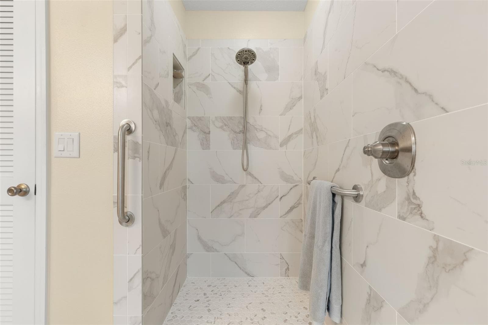 A closer look at the beautifully updated primary shower reveals striking tile, a pebble-style floor, built-in niche, and handheld showerhead, creating a refreshing escape with a touch of modern elegance. - 19 EDGELY LN, PALM COAST