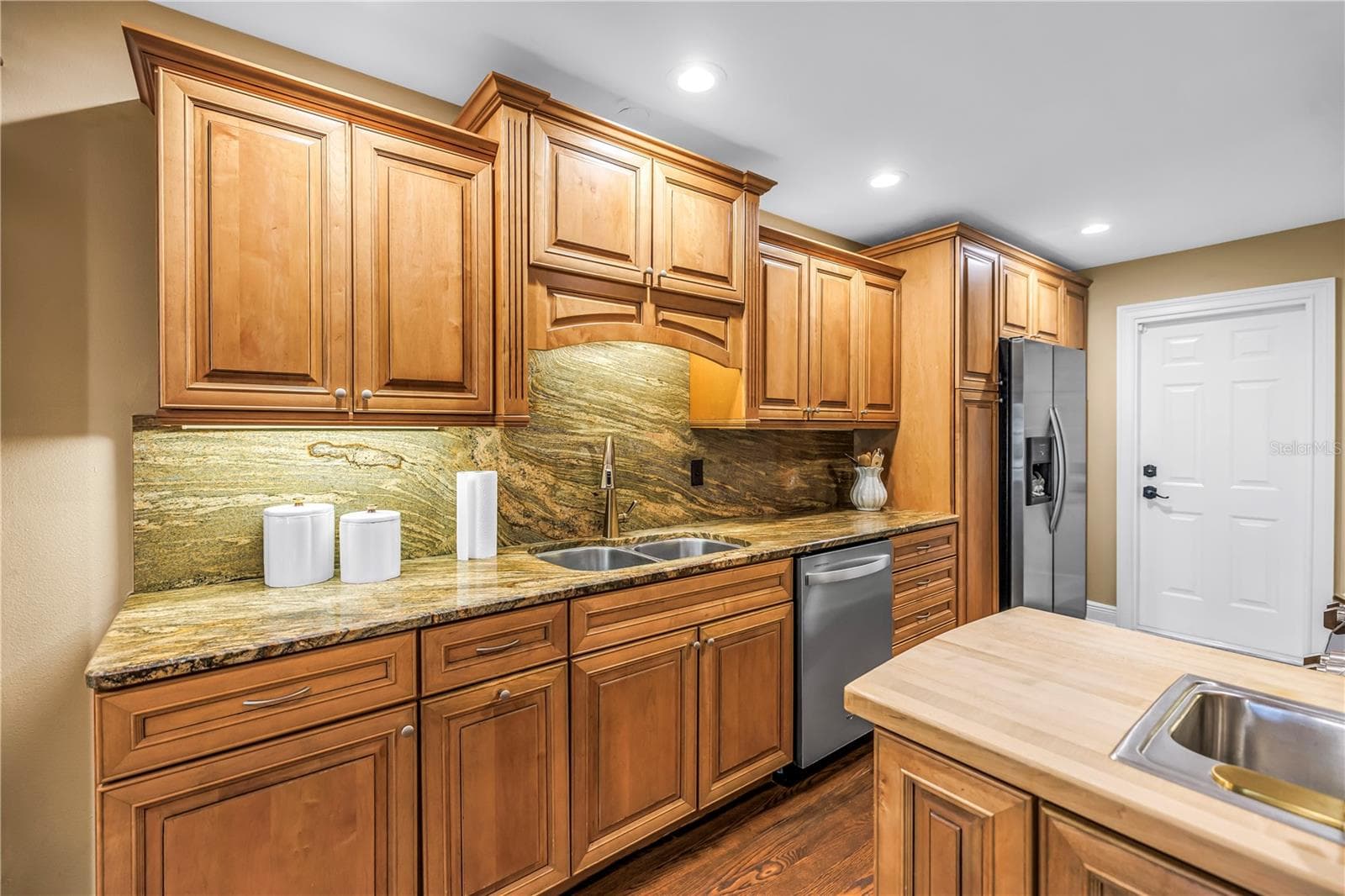 This custom kitchen features solid wood cabinetry, granite countertops, and a matching backsplash. It is equipped with updated stainless steel appliances, a chopping block island, and an integrated prep sink. An ideal space for any culinary enthusiast. - 868 GLADES CT NE, ST PETERSBURG