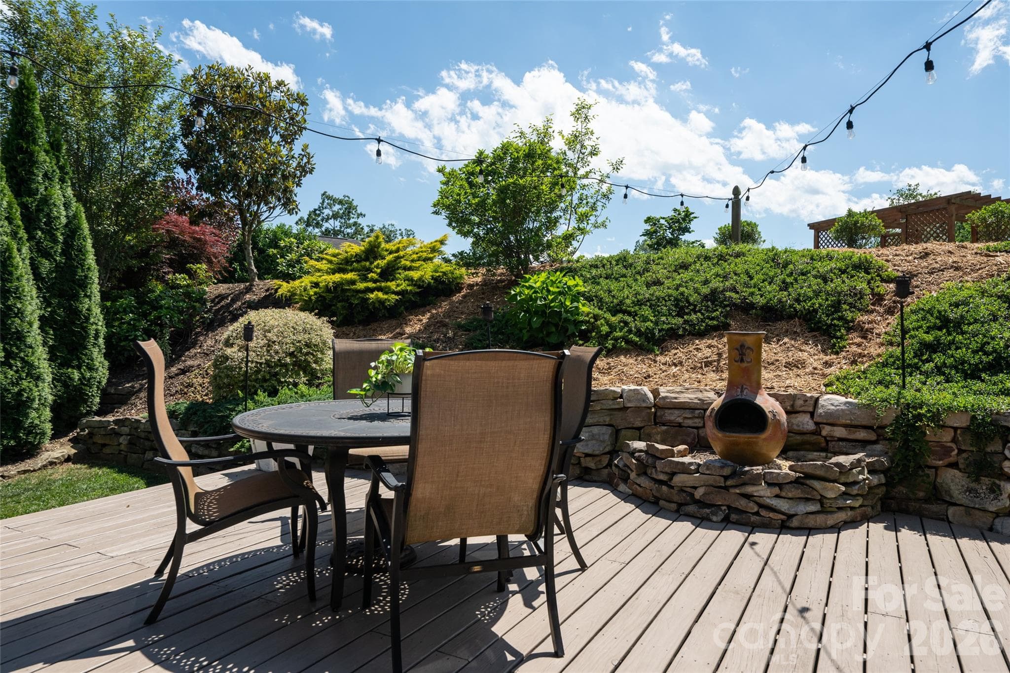 Private rear deck with outdoor dining space and string lighting, backed by a stone-terraced landscaped slope. - 17 Asher Lane, Arden