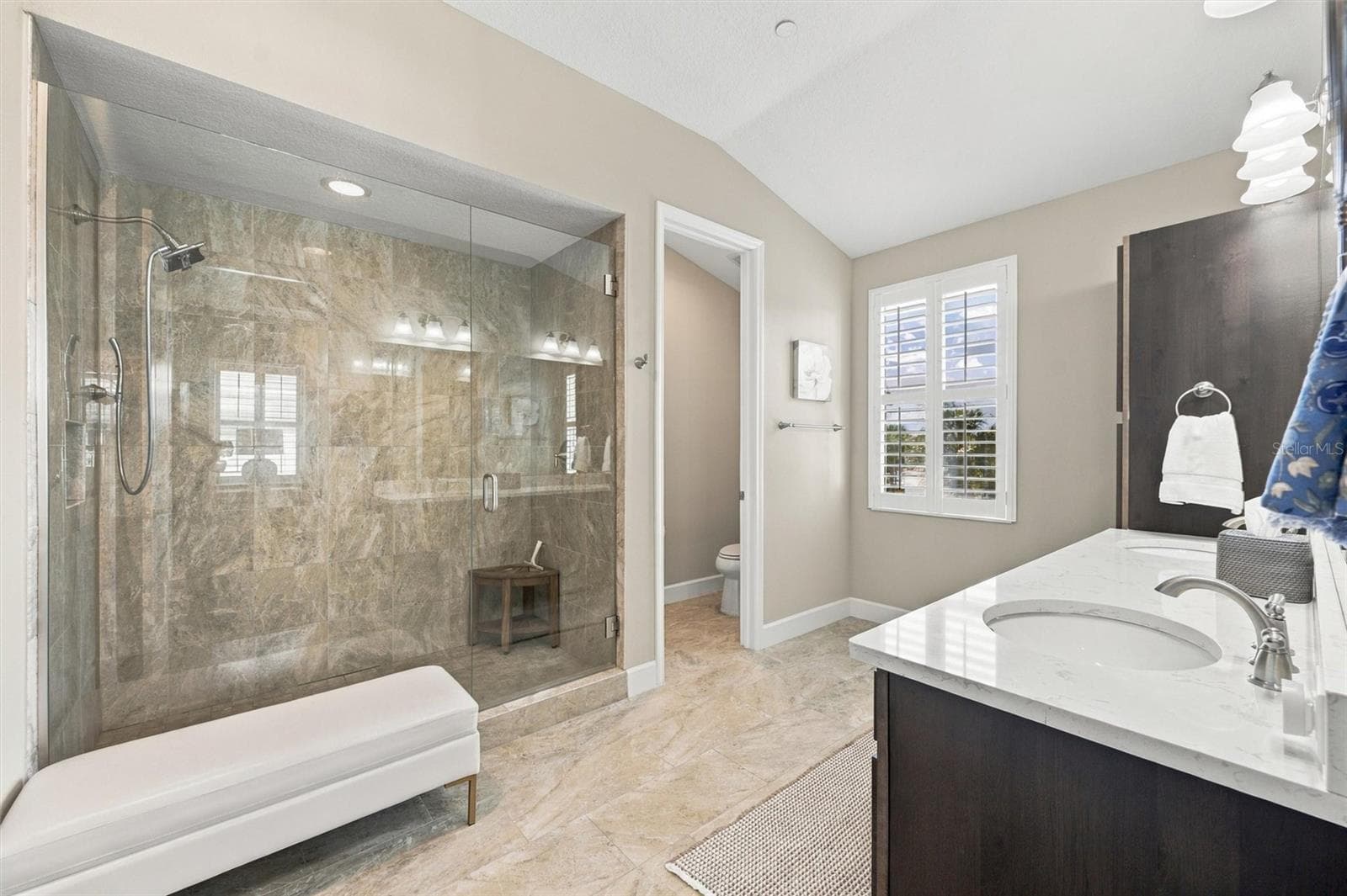 The spacious primary ensuite features dual vanities, a large walk-in shower, a private water closet, and convenient access to one of the suite’s two walk-in closets. - 291 COMPASS POINT DR #201, BRADENTON