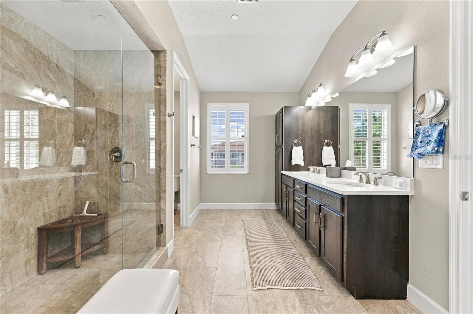 The spacious primary ensuite features dual vanities, a large walk-in shower, a private water closet, and convenient access to one of the suite’s two walk-in closets. - 291 COMPASS POINT DR #201, BRADENTON