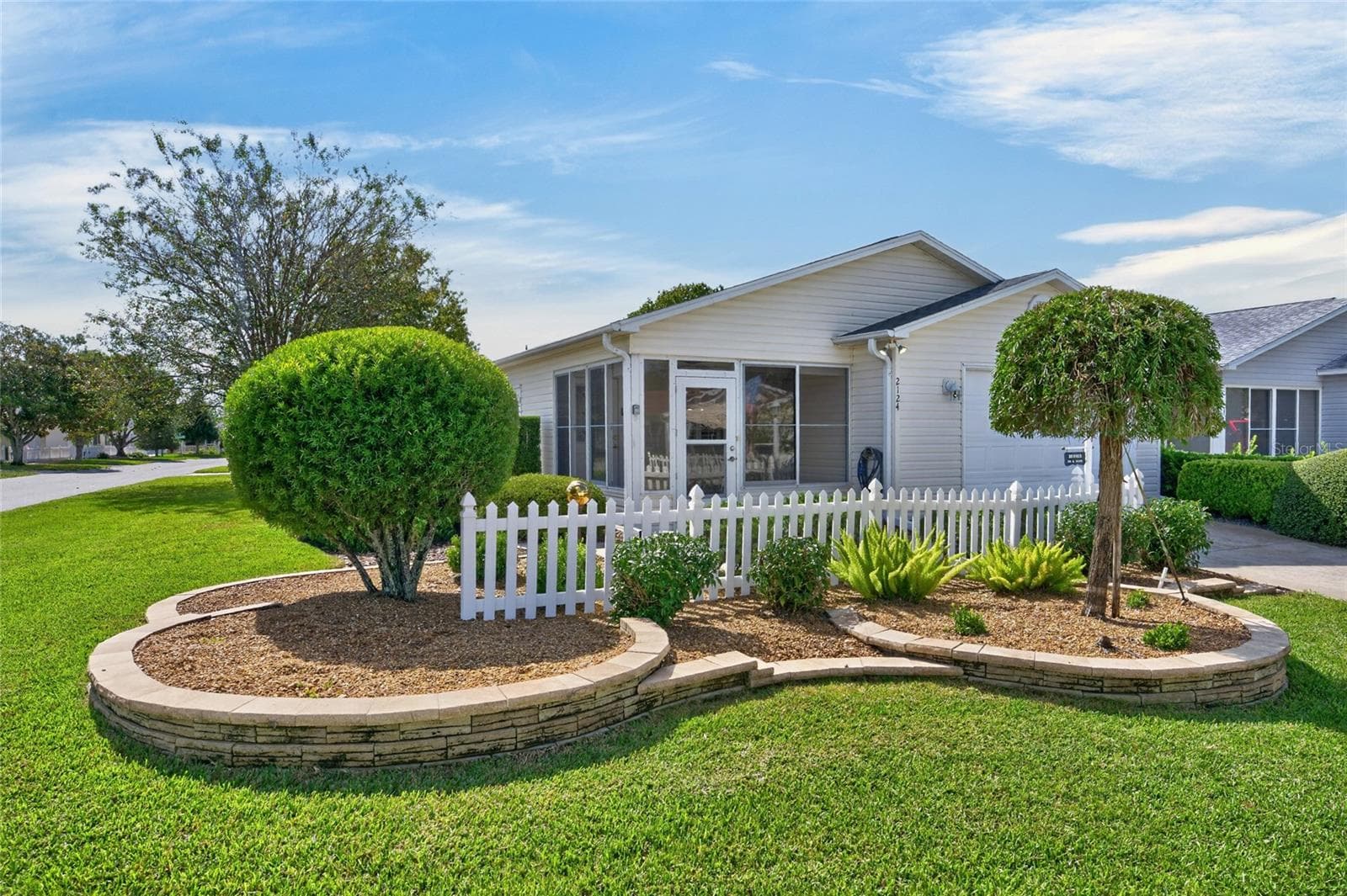 FRONT EXTERIOR - Elevated STACKED STONE landscape beds, manicured mature landscaping and a white PICKET FENCE frame the enclosed front lanai. - 2124 ESCOBAR AVE, THE VILLAGES