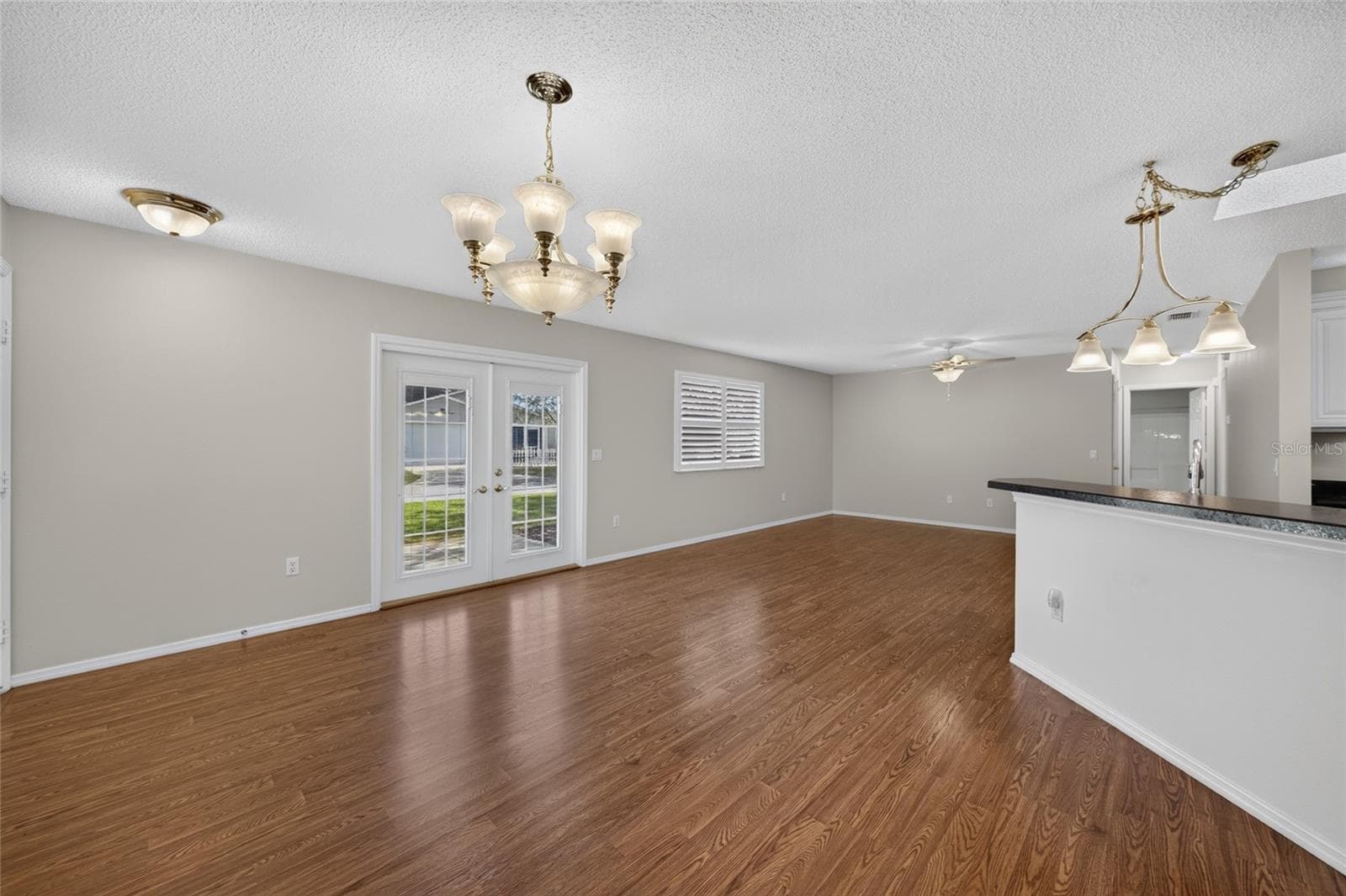 Overview of DINING / KITCHEN/LIVING ROOM - A dining chandelier, breakfast-bar pendant and a new ceiling fan w/ alabaster-white bowl coordinate the lighting across the connected spaces. - 2124 ESCOBAR AVE, THE VILLAGES