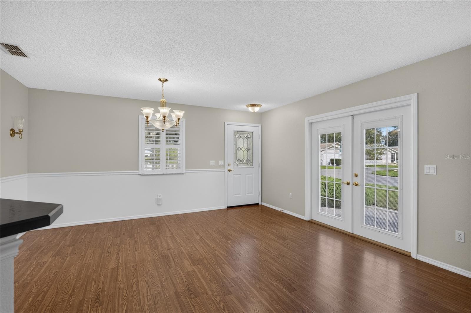 Close up view of DINING ROOM - Chair rail woodwork, decorative wall sconces (back L), and matching chandelier & pendant lighting add distinctive detail. Note the French doors which access the side patio on eastern side of home. - 2124 ESCOBAR AVE, THE VILLAGES