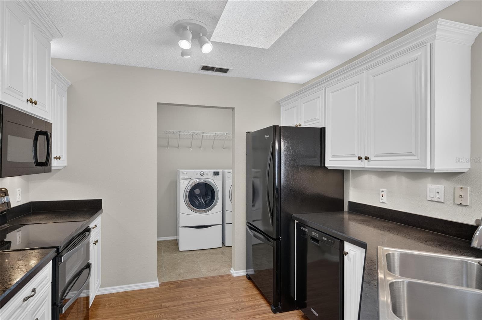 KITCHEN View - Showcases raised-panel white cabinetry with crown molding and over & under cab lights. A SKYLIGHT illuminates the kitchen w/ NATURAL LIGHT. Note that black appliances provide a dramatic contrast of color. - 2124 ESCOBAR AVE, THE VILLAGES