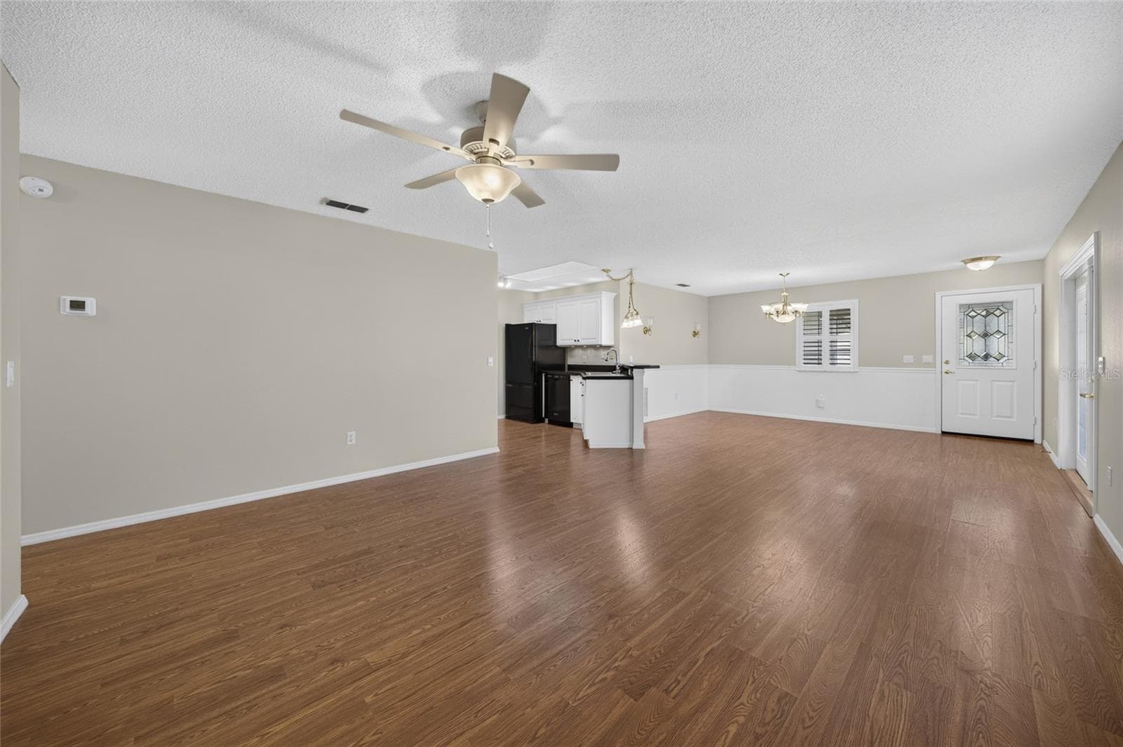 View from back of LIVING ROOM - Shows an alternate view of the main living area - LIVING ROOM (front), KITCHEN (center L), and DINING ROOM (across back) - 2124 ESCOBAR AVE, THE VILLAGES