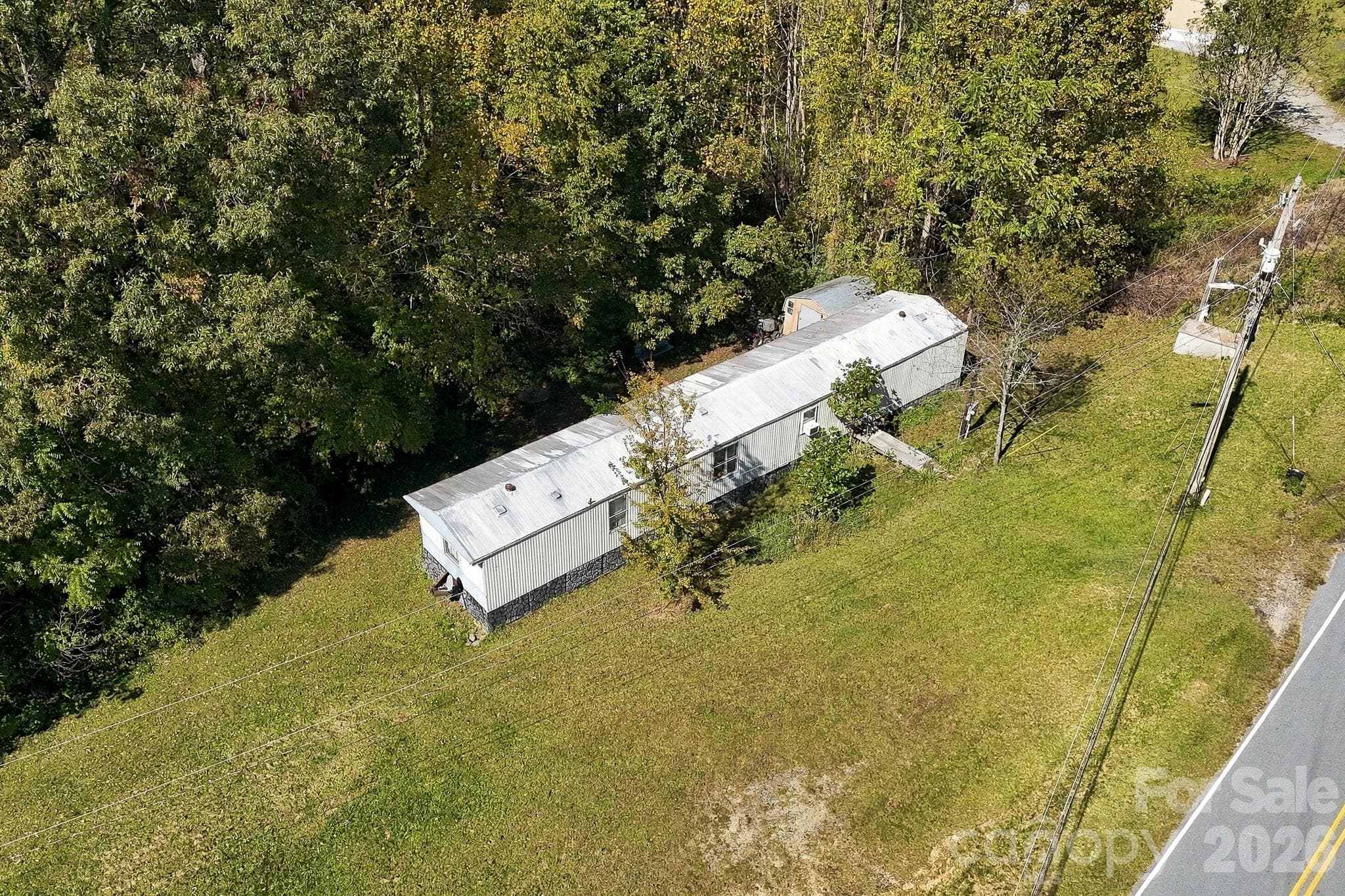 Existing mobile home positioned near the paved road, with a grassy yard and mature trees providing a scenic backdrop. - 631 Union Hill Road, Hendersonville