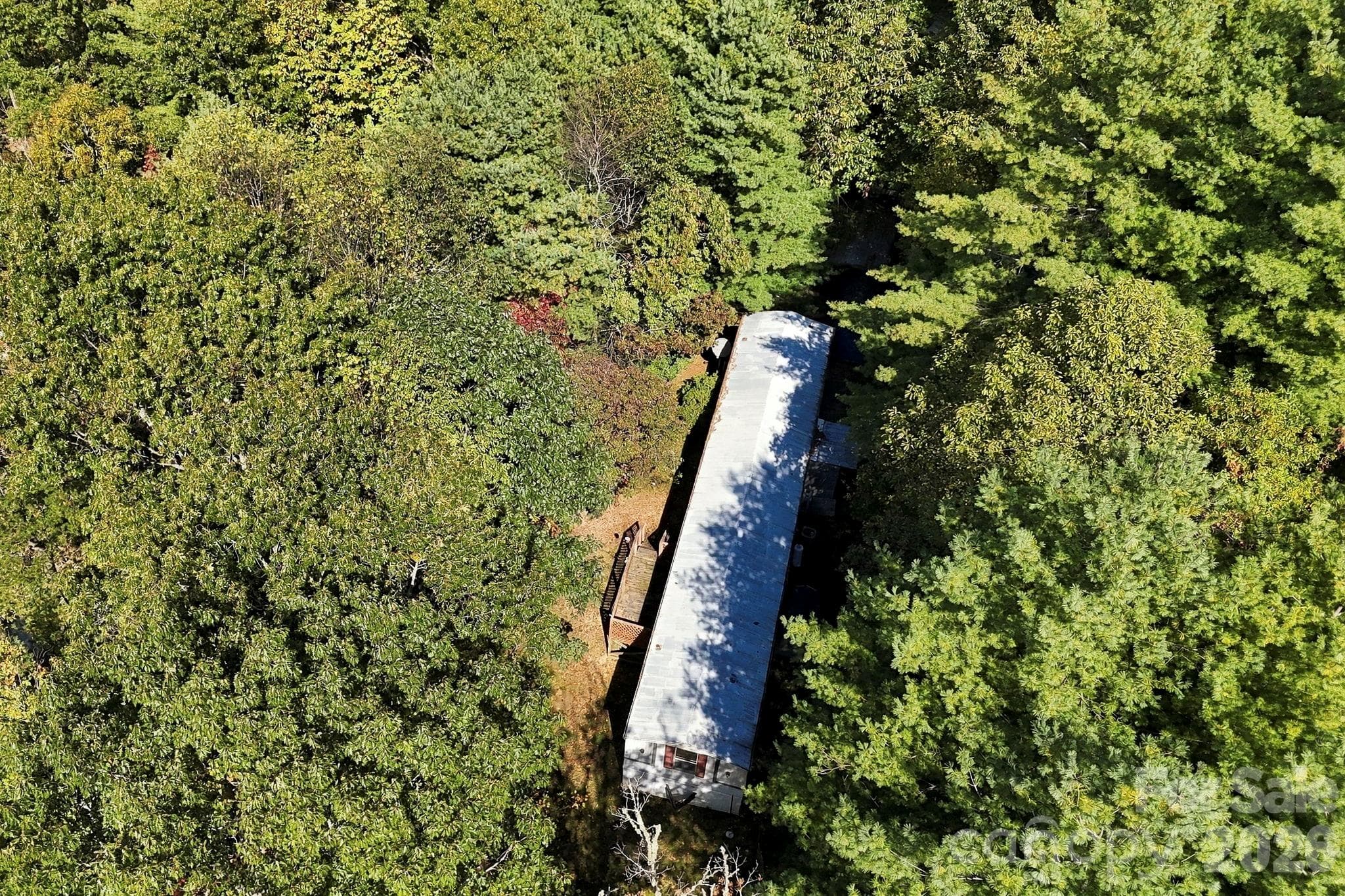 Mobile home nestled among mature trees, showcasing the natural privacy and established residential use of the property. - 631 Union Hill Road, Hendersonville
